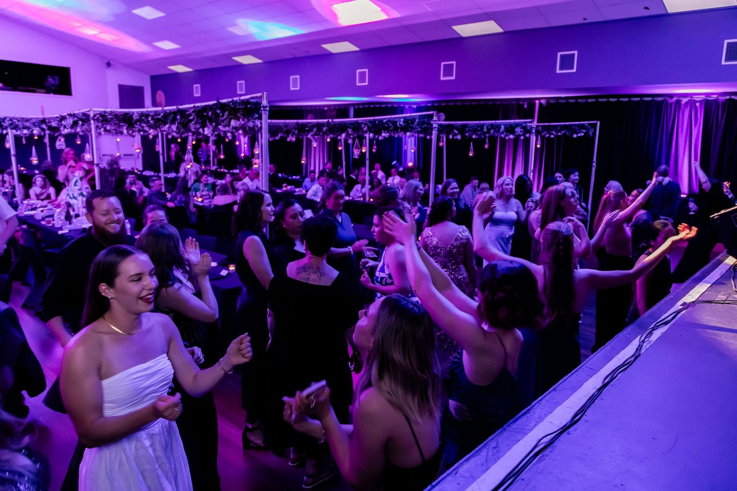 Crowded dance floor with purple and blue lighting at formal event.