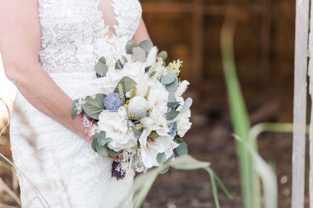 A wedding dress detail photo showing a delicate lace bodice and bouquet with white and pink florals.