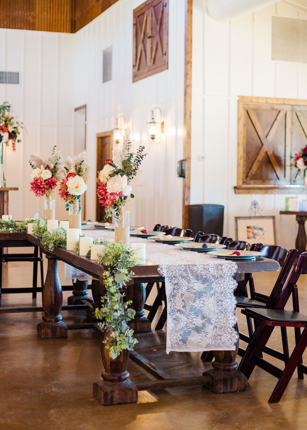 Wedding reception setup with dark wooden chairs and white lace table decorations.