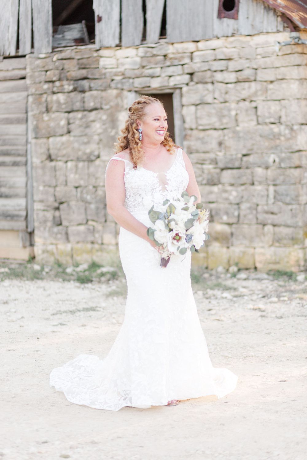 Rustic outdoor bridal portraits against a stone wall backdrop featuring a flowing white wedding dress.