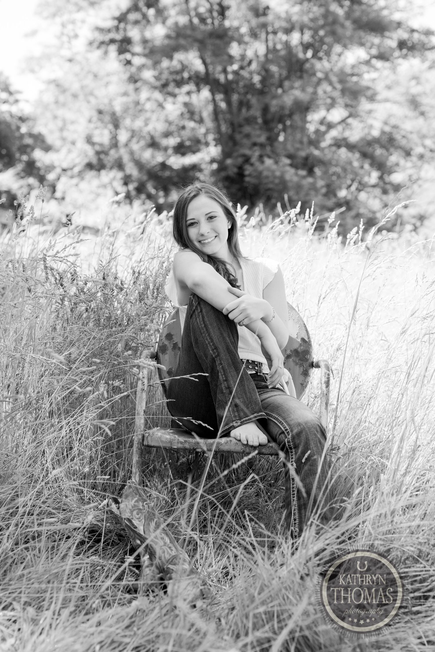 Black and white artistic portrait in rustic setting with antique chair surrounded by wild grass.