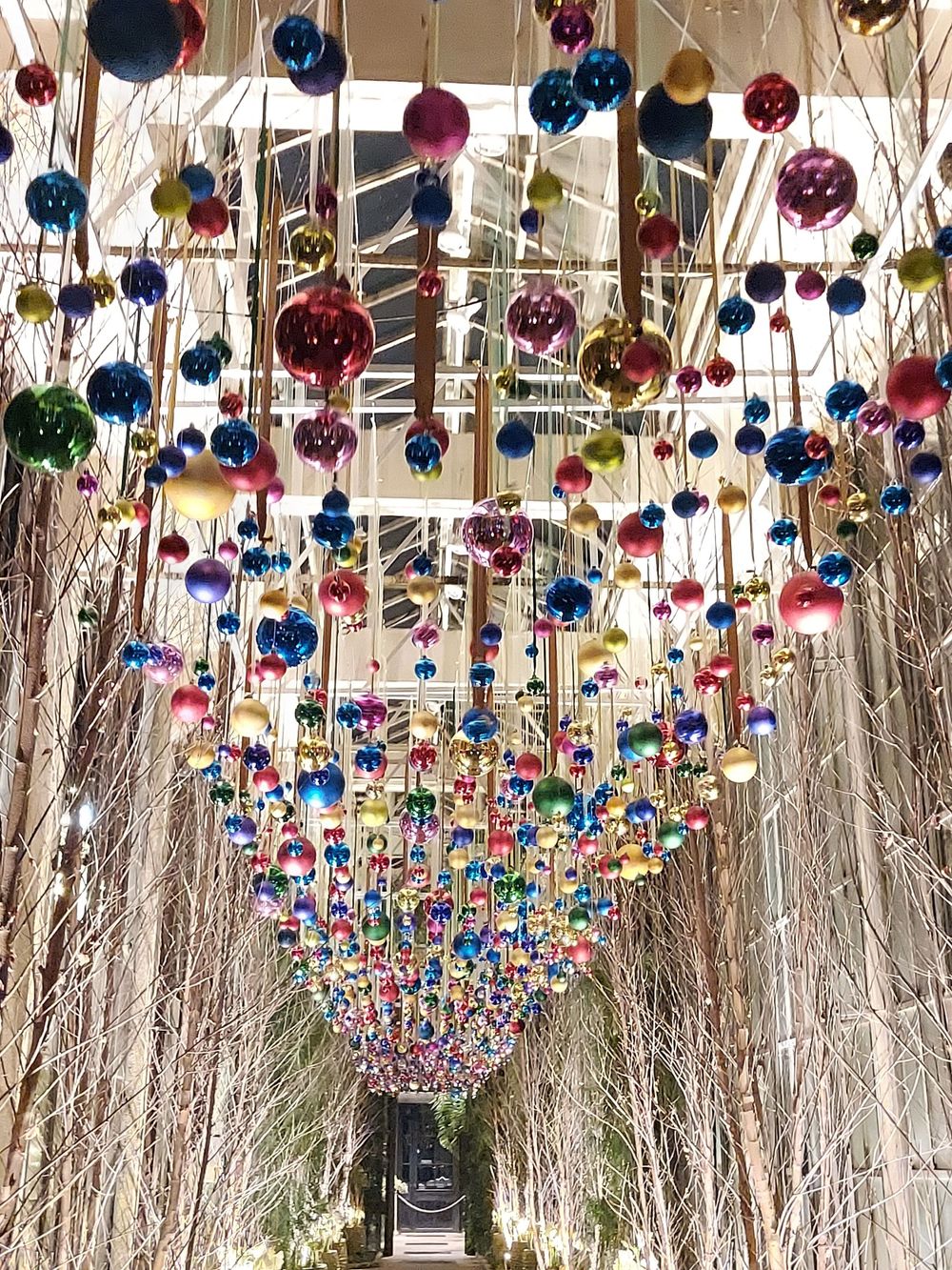 Colorful hanging Christmas ornaments create a tunnel effect with shimmering baubles in blue, pink, and gold.