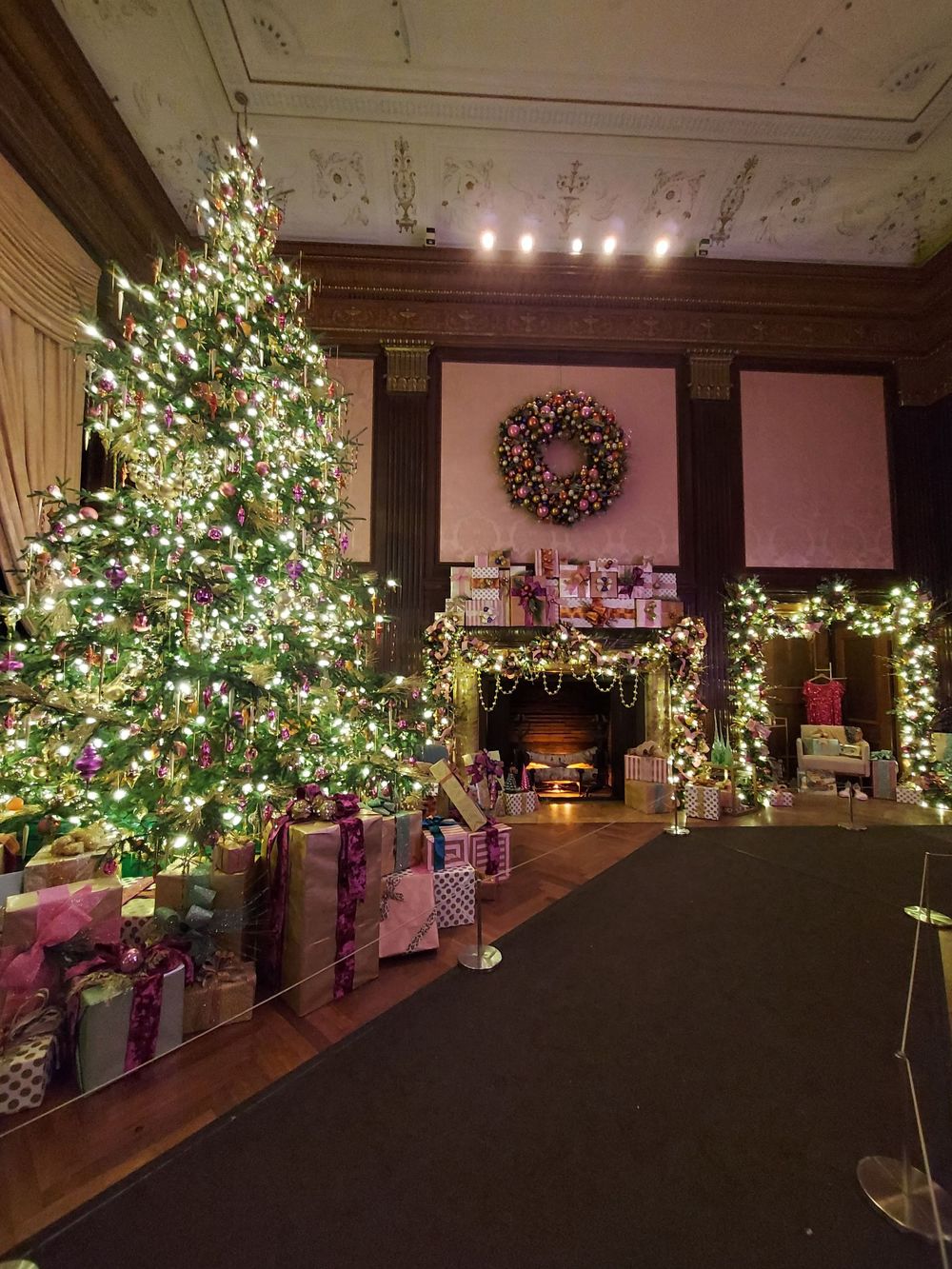 Elegant Christmas tree with white lights and wrapped presents in front of a decorated fireplace.