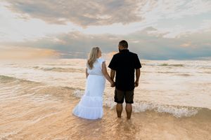 Couple walking together on beach at sunset with waves crashing behind them.