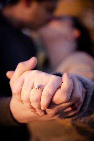 Close-up shot of hands with engagement ring in soft lighting.