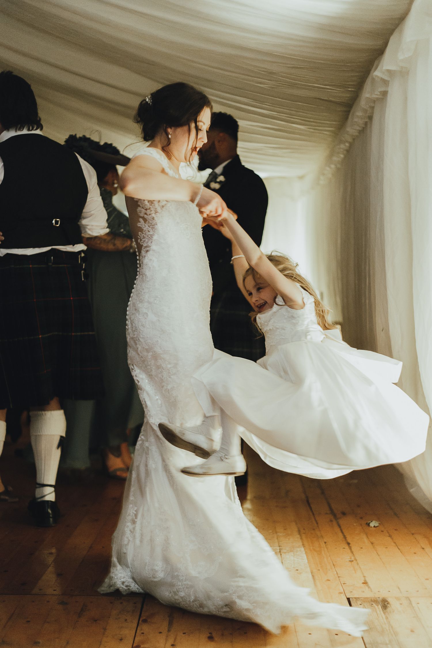 Two dancers in white dresses perform a dramatic dance move during a wedding reception.
