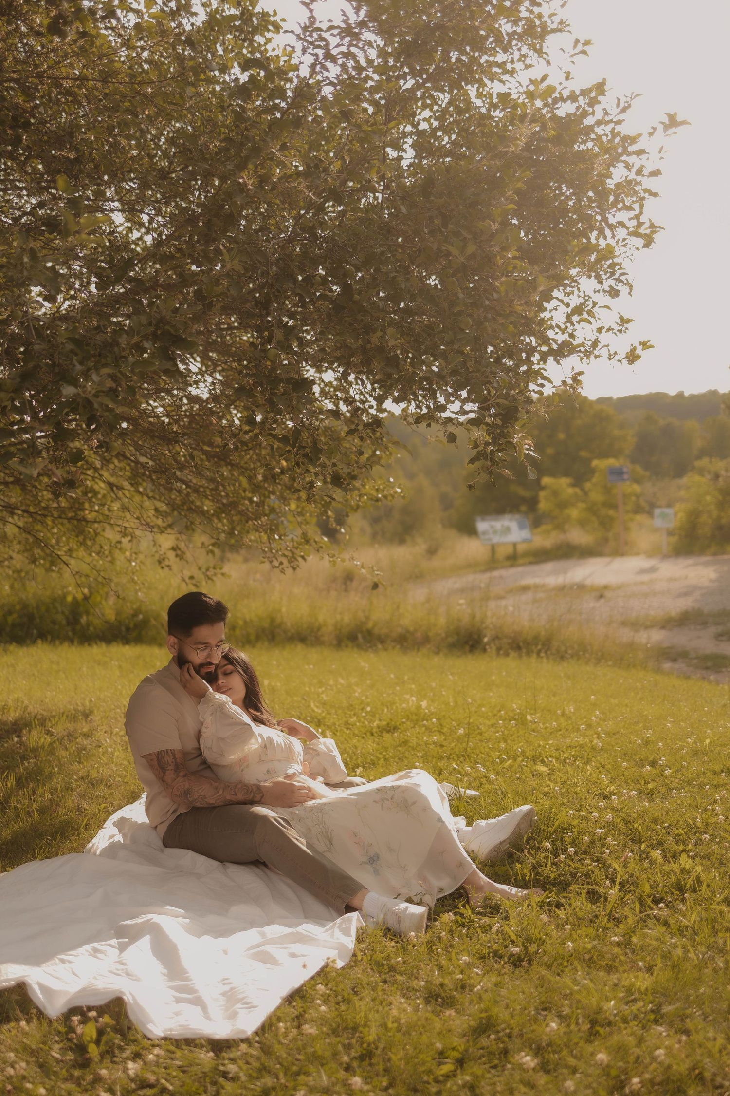 Couple relaxing on white blanket under tree in sunny meadow.