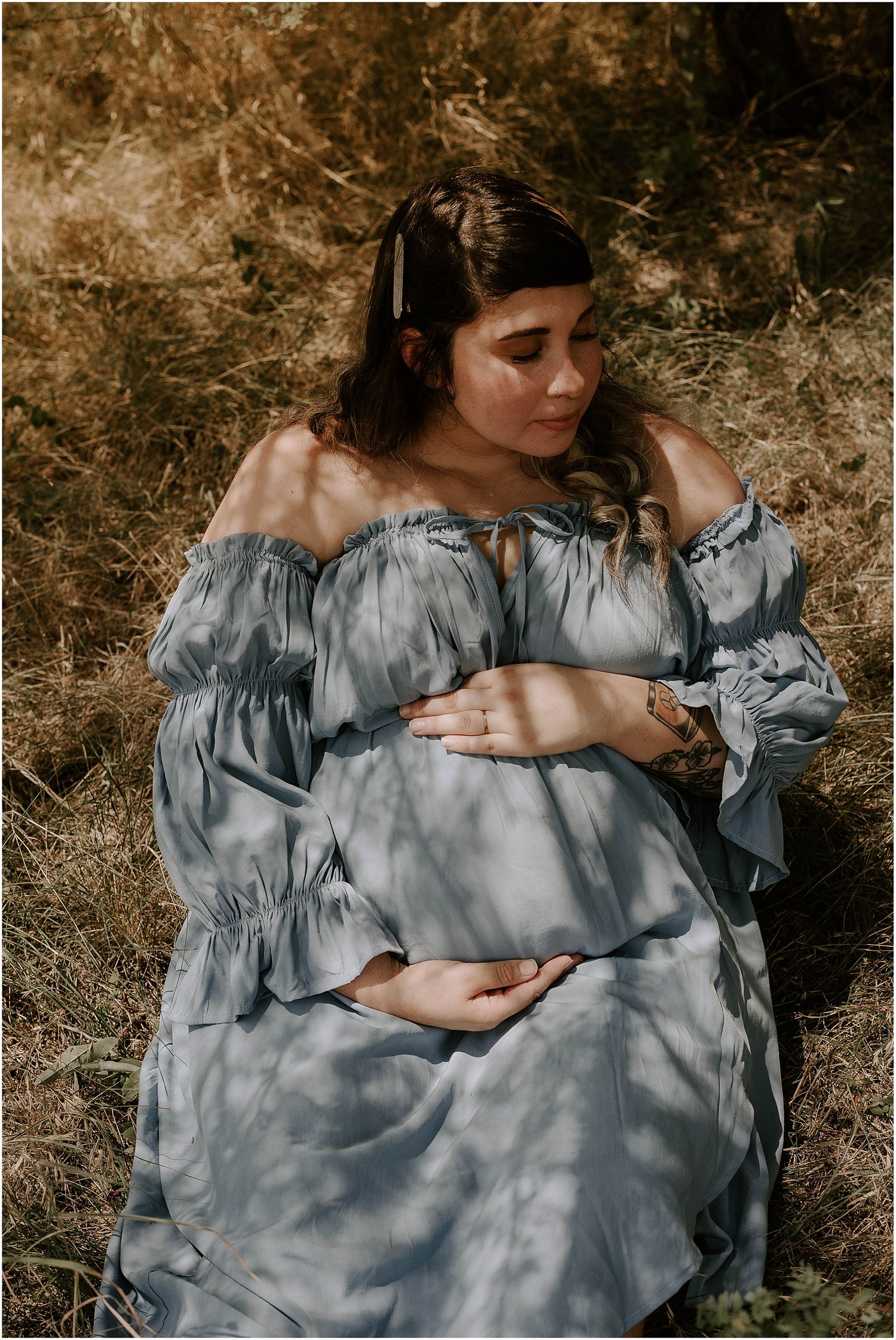Intimate maternity photograph with soft lighting highlighting a flowing grey dress and gentle expression.