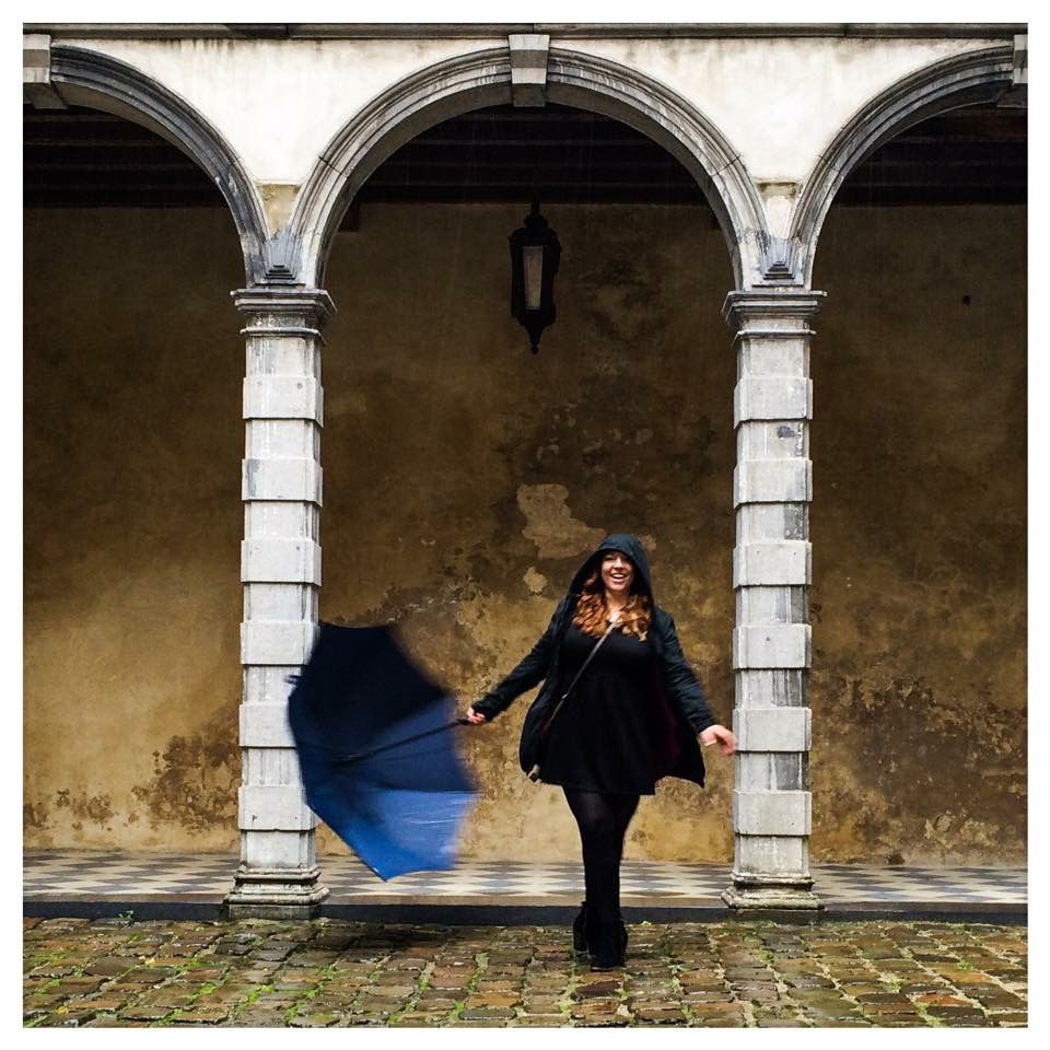 Artistic photo of a person in black dress twirling under stone arches with a blue motion blur effect.