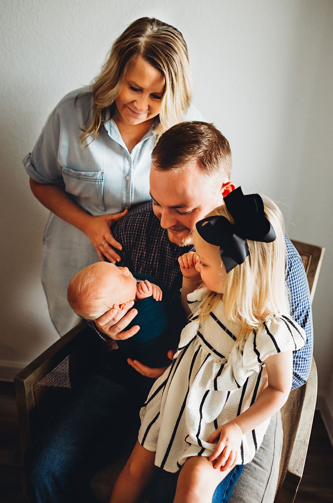 A candid family moment shows parents with their baby and young daughter sharing loving smiles together in a natural setting.