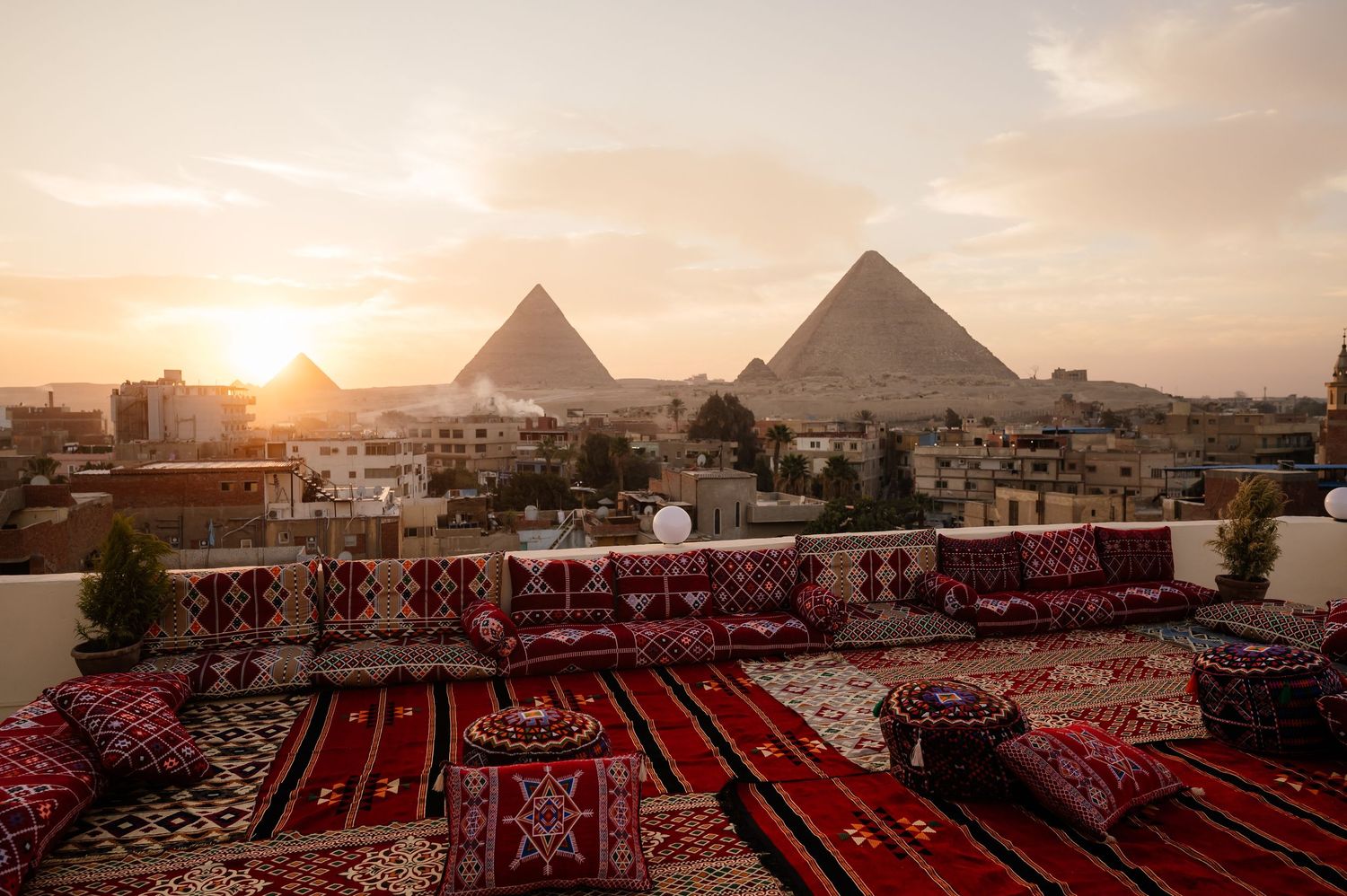Sunset view of the Pyramids of Giza with traditional carpets and cushions in foreground.