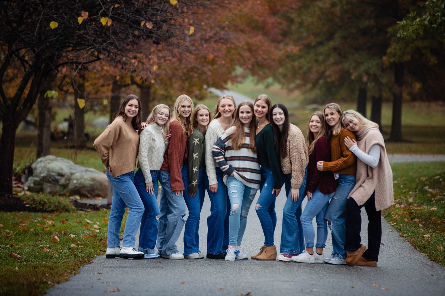 Group photo of friends wearing jeans and sweaters posing together on a path during autumn.