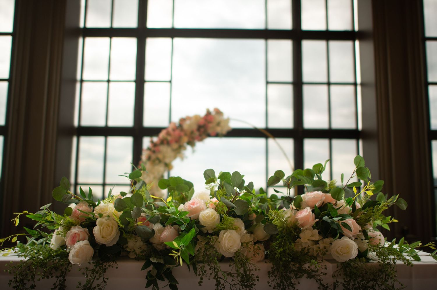 Elegant floral arrangement with white flowers and greenery decorating a windowsill in natural light.