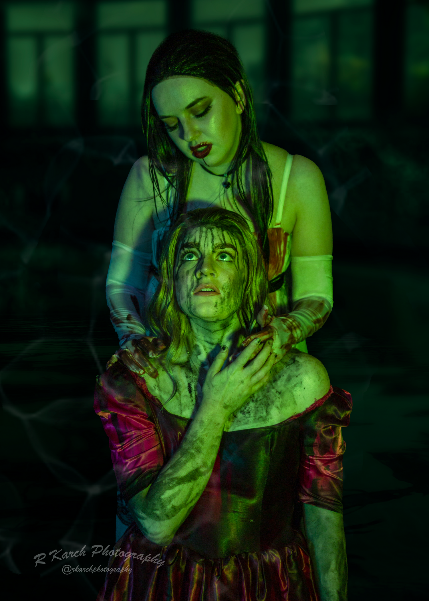 Dark theatrical scene with two performers in period costume under green illumination.