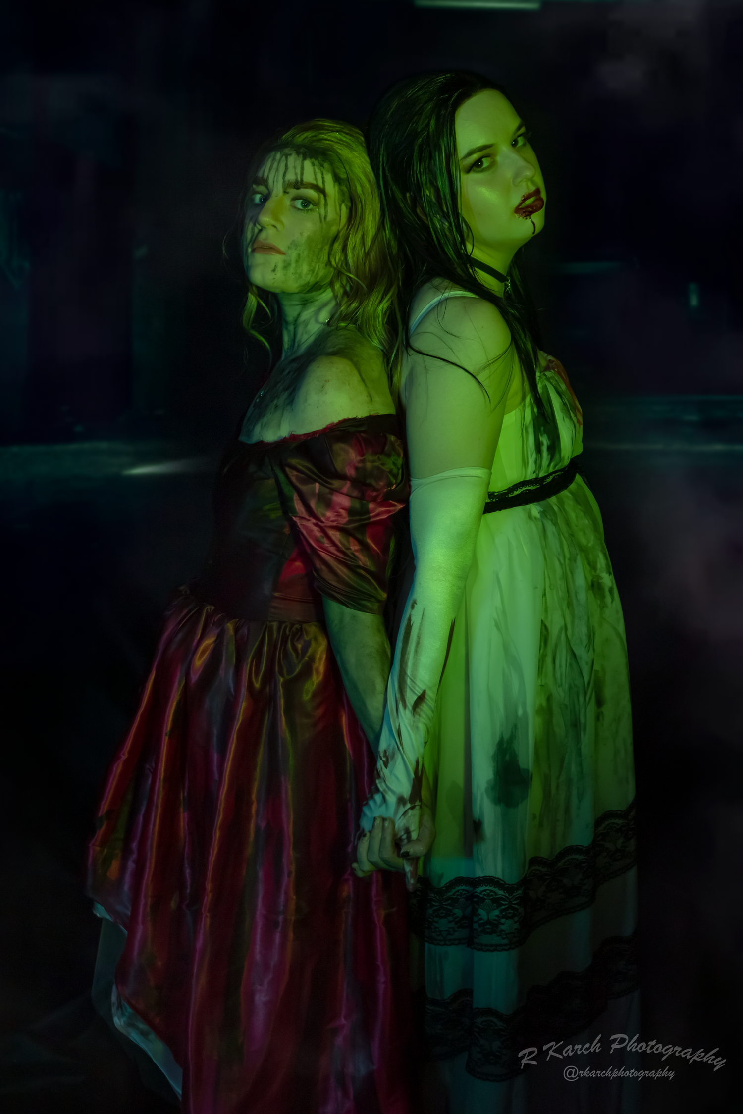 Artistic portrait of two figures in vintage dresses with moody green lighting.