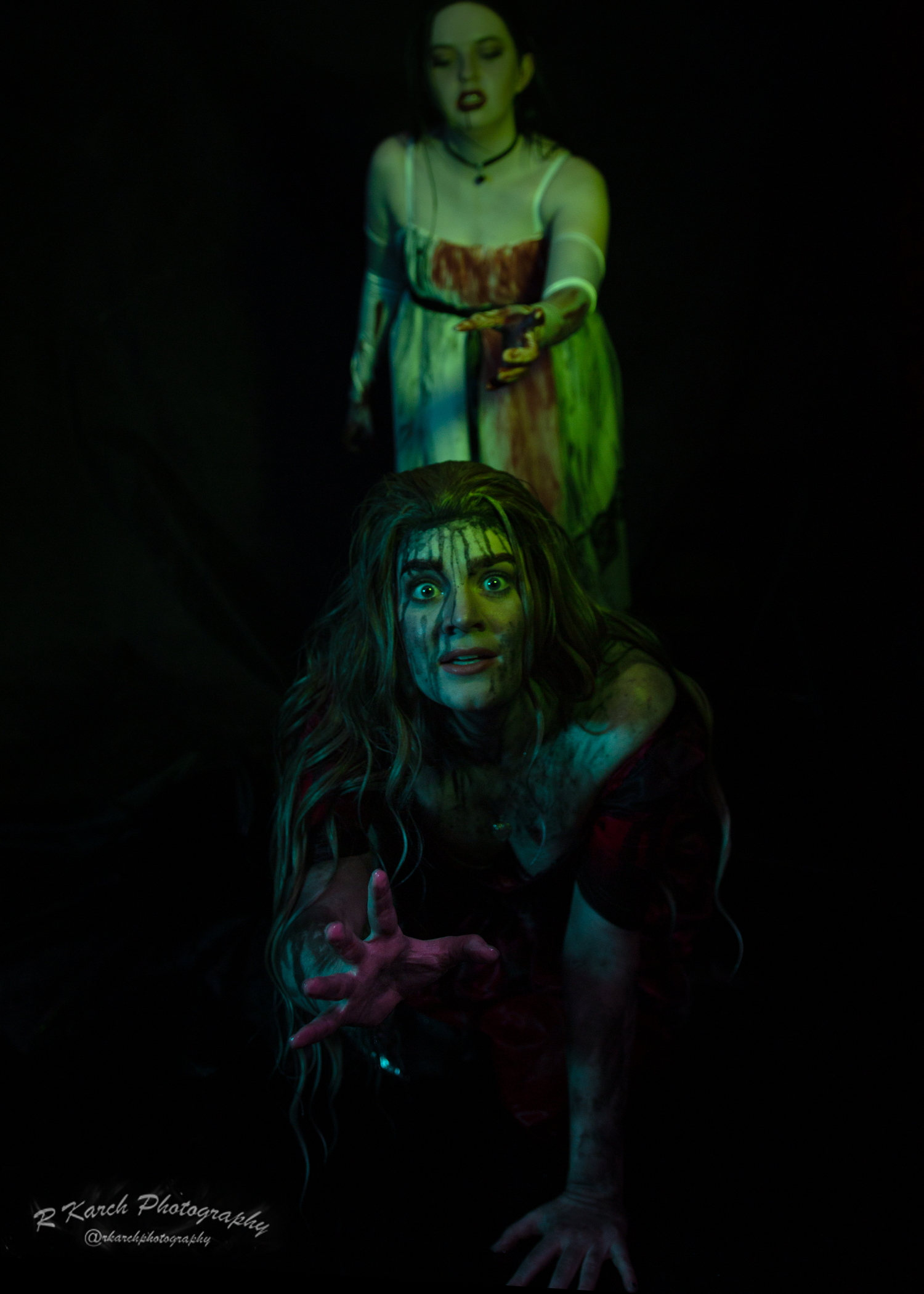 A haunting scene with two women in period costumes illuminated by ghostly green light.