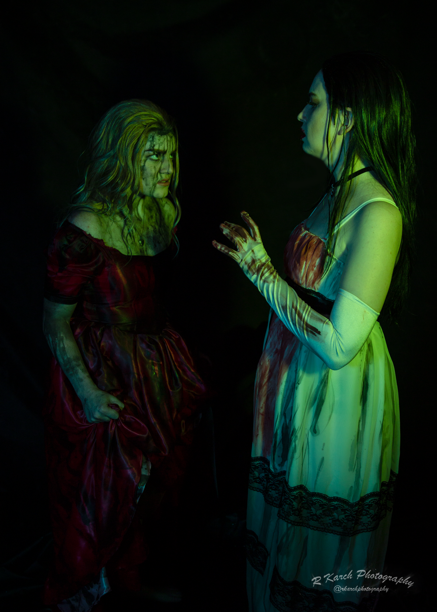 Gothic horror scene shows two performers in period clothing gesturing dramatically under green light.