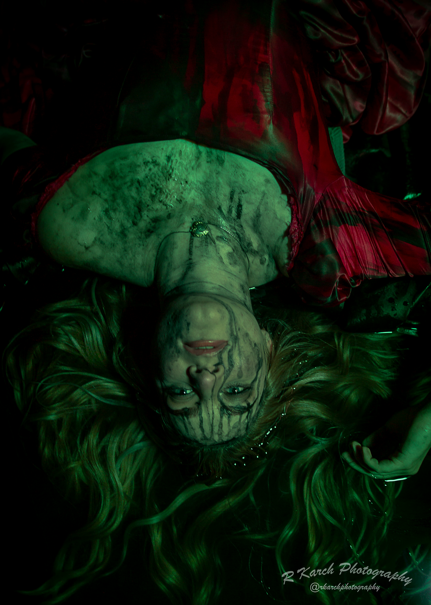 Inverted horror scene featuring performer with long hair in vintage dress under green lighting effects.