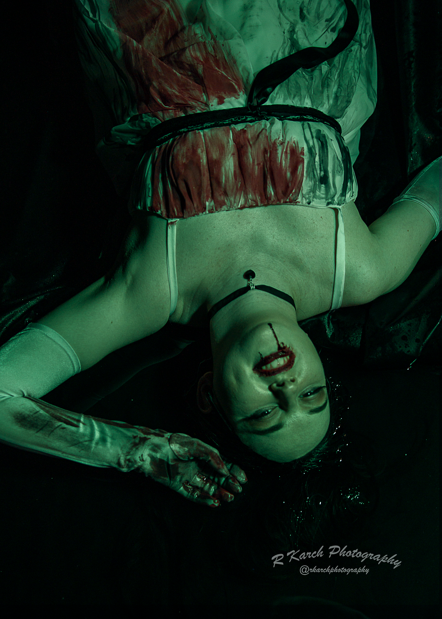 Artistic horror photography features inverted figure in vintage dress under green lighting.