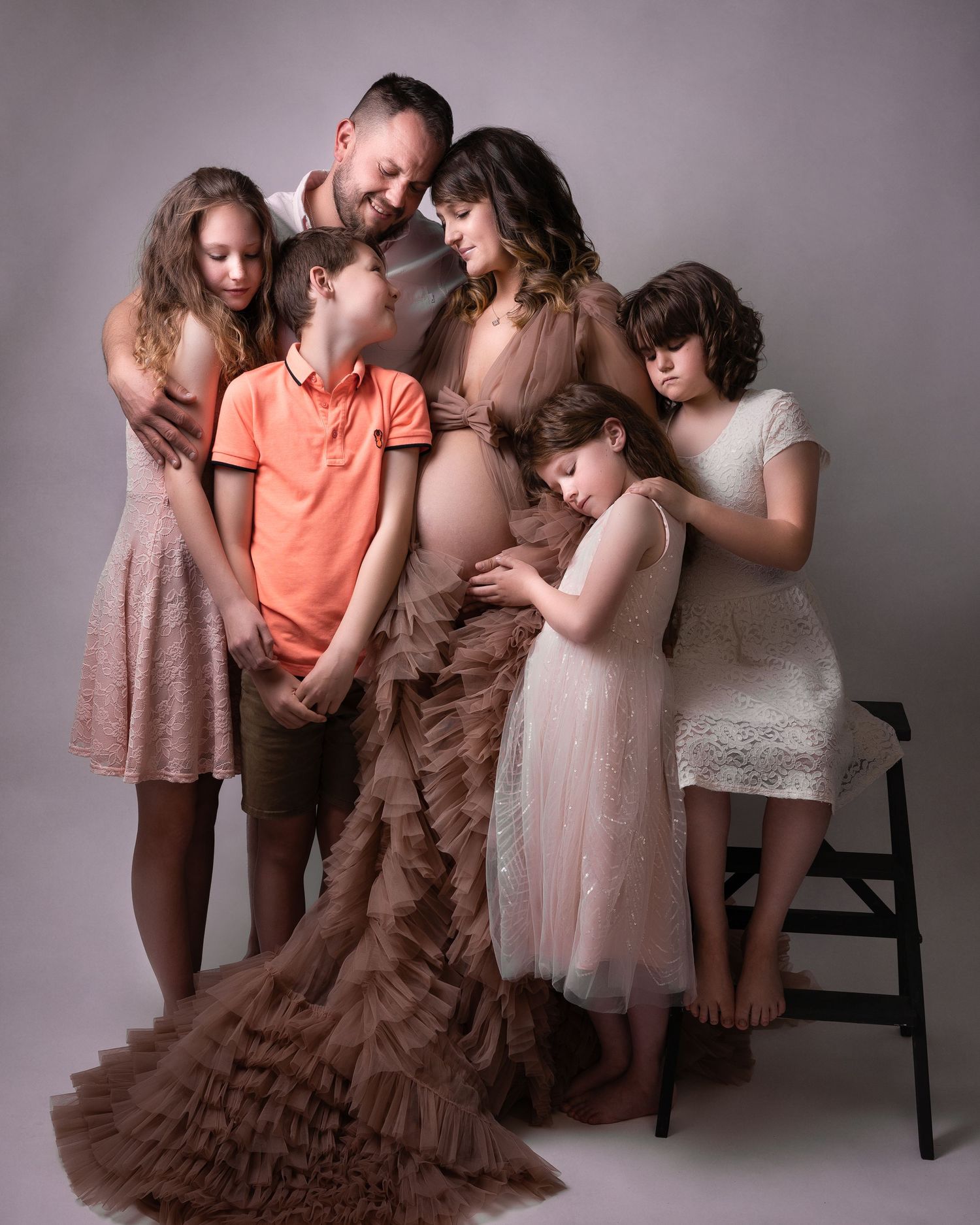 Family maternity portrait with children gathered around in soft pink and neutral tones.