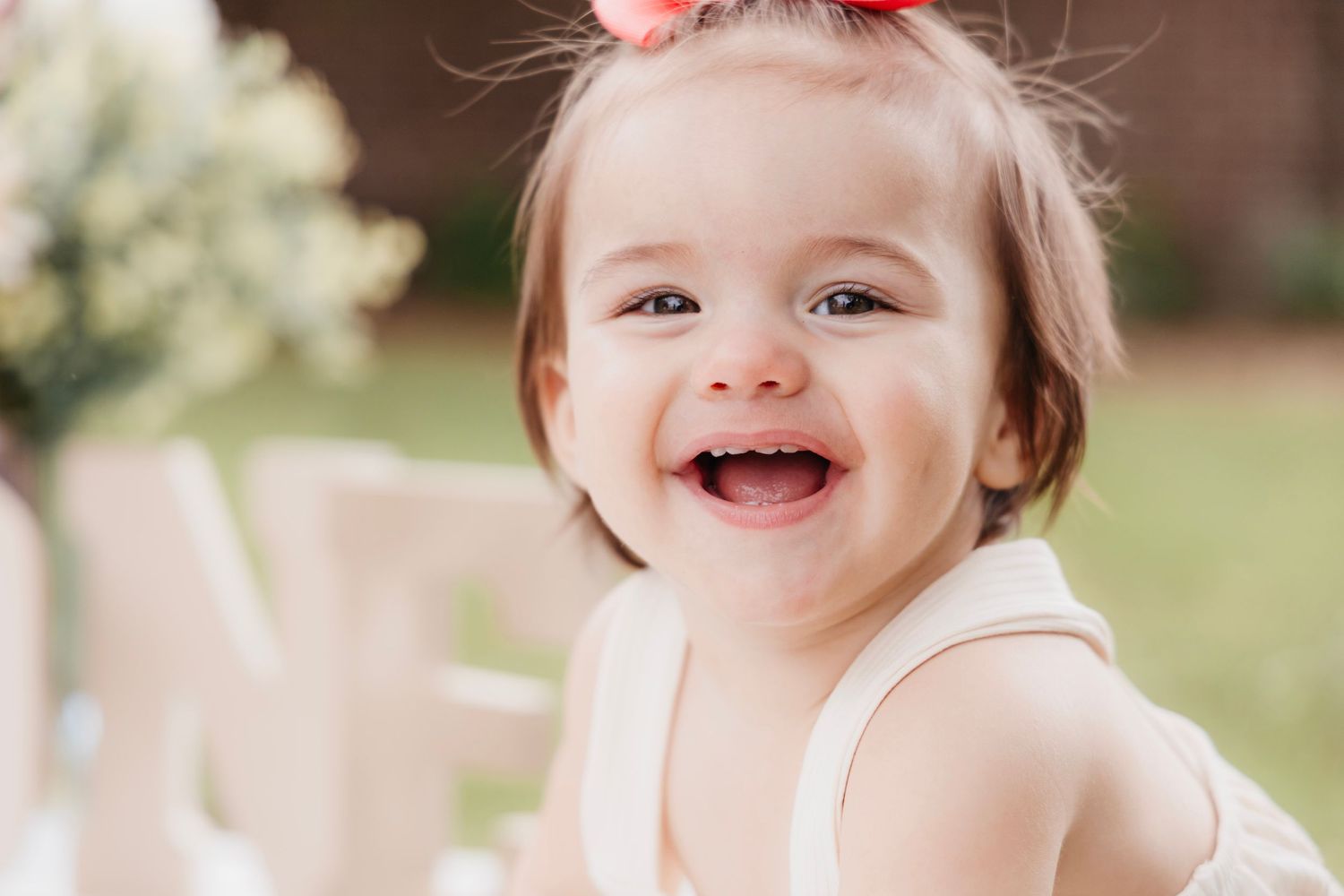 Baby with pink bow smiling brightly in outdoor portrait session.