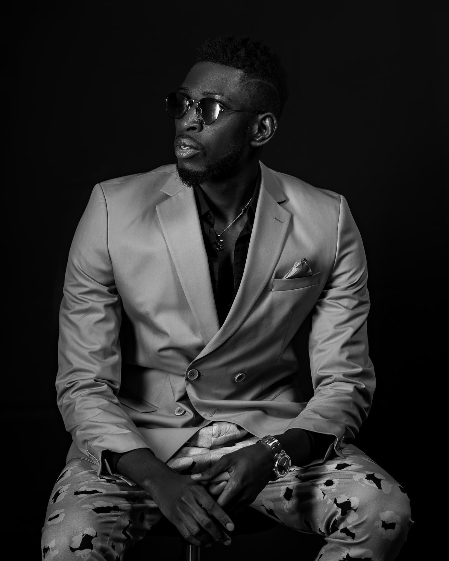Stylish studio portrait of a man in glasses and light blazer against black background.