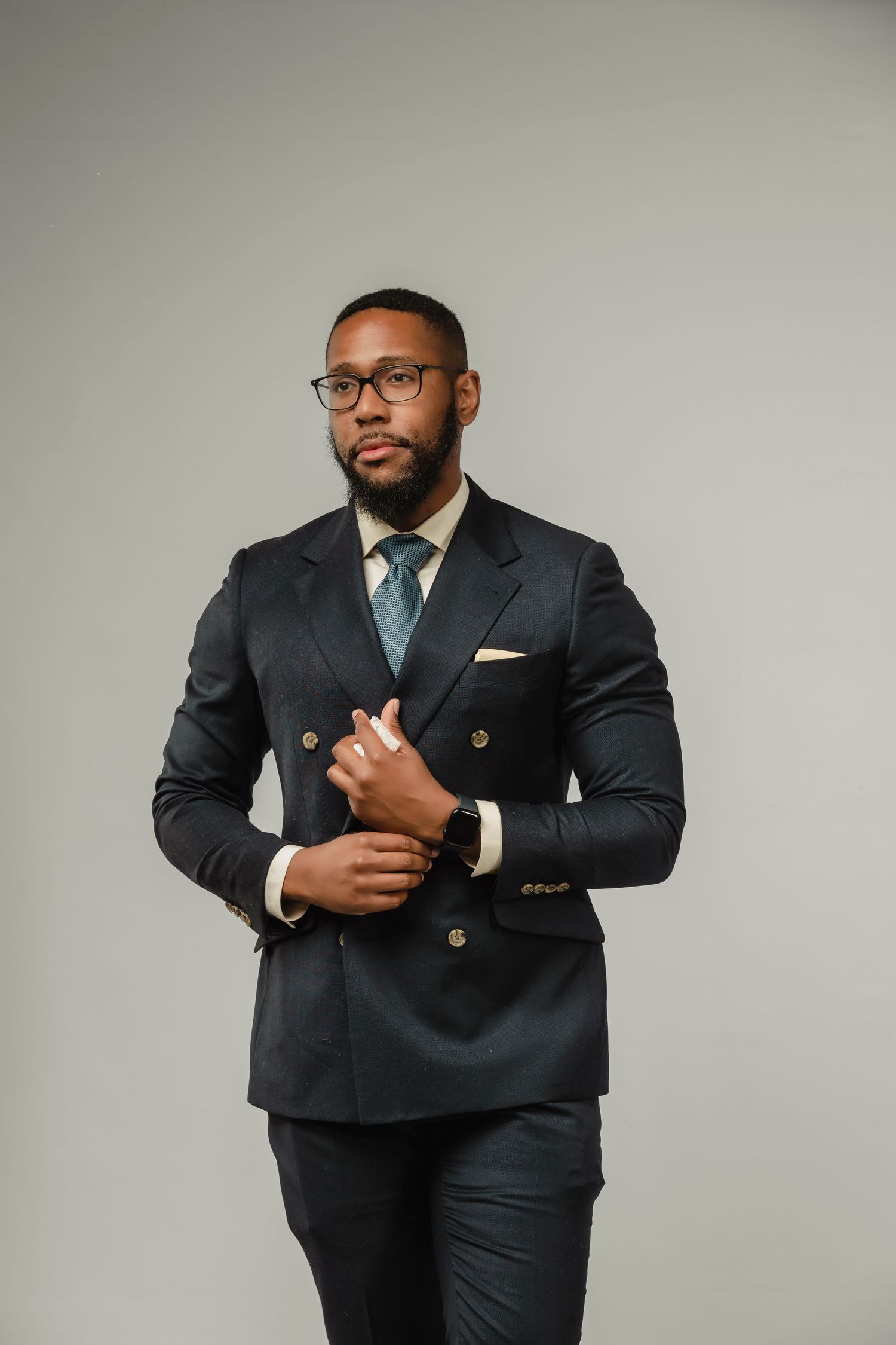 Professional wearing a dark suit stands confidently against neutral background in elegant portrait series.