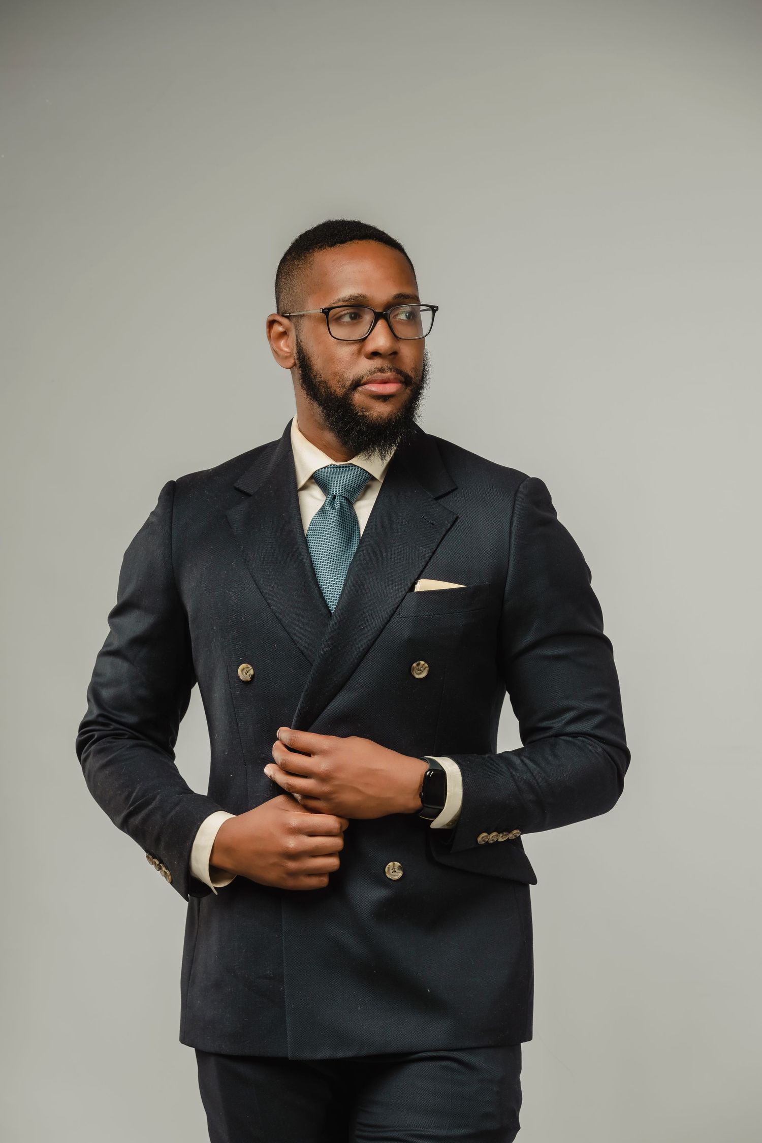 Professional portrait of someone wearing a navy double-breasted suit and glasses against a light gray backdrop.