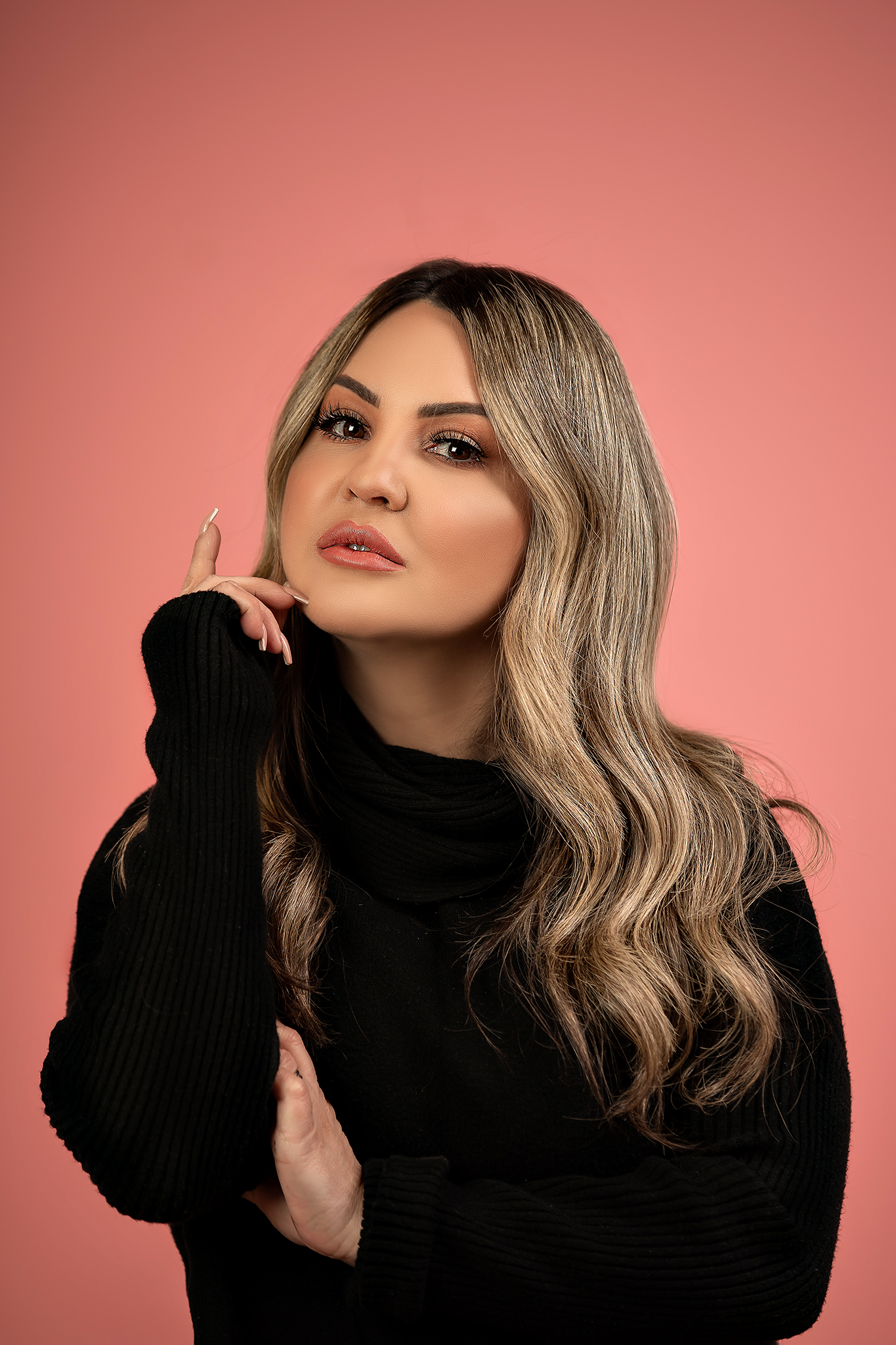 Studio portrait featuring black turtleneck sweater and flowing blonde hair against coral background.