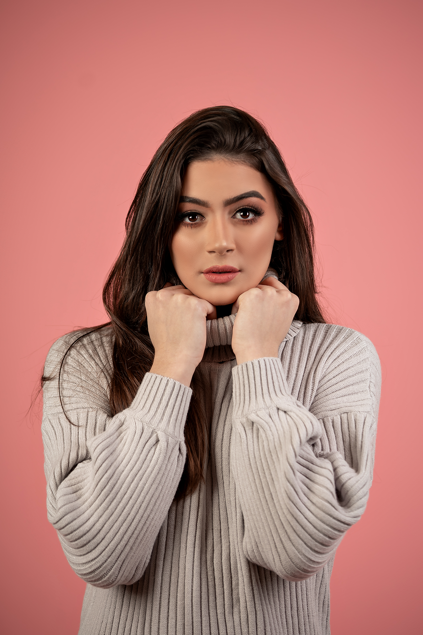 Portrait against pink backdrop showcases cozy grey ribbed turtleneck sweater in studio lighting.