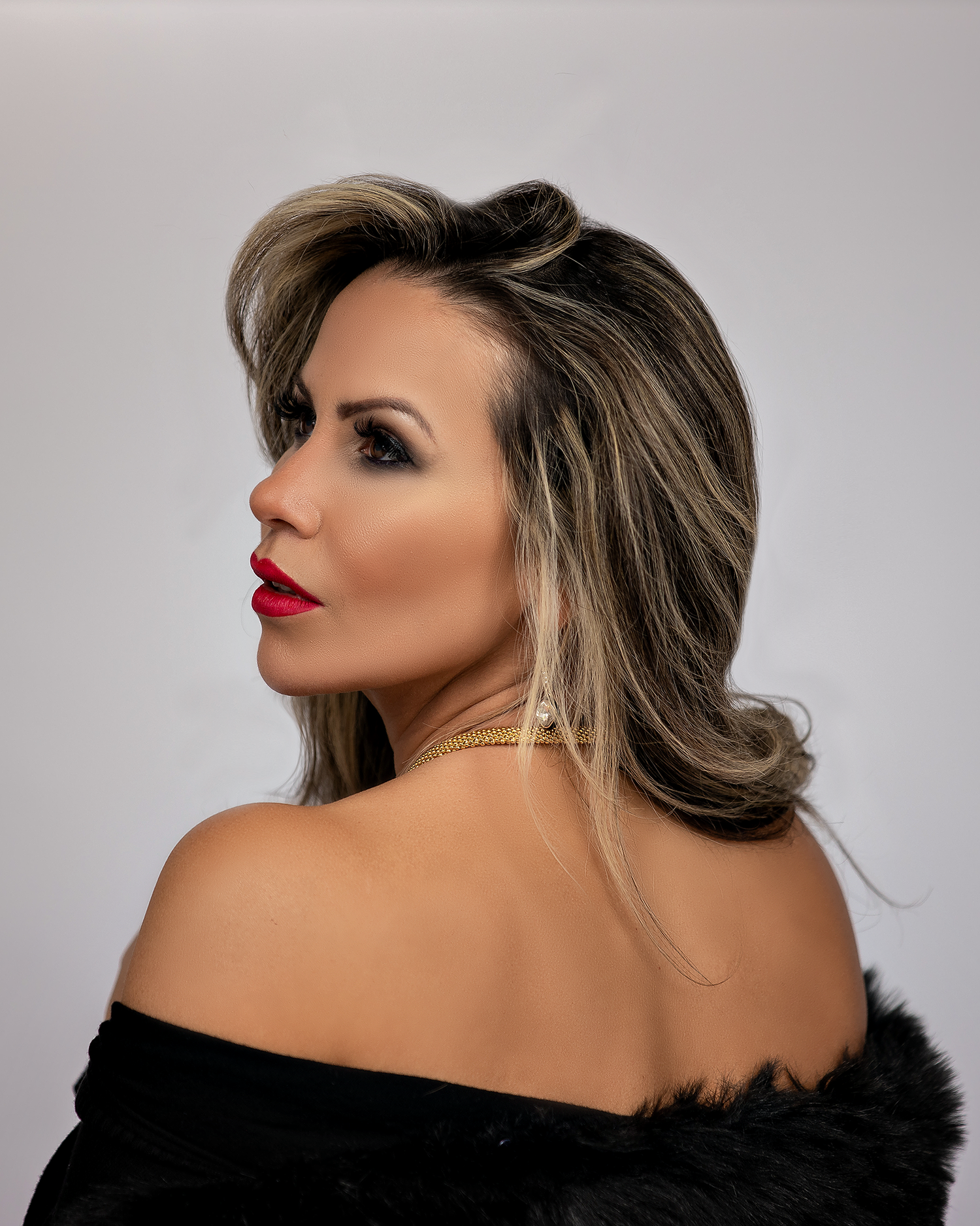 Glamorous portrait with off-shoulder fur top and classic red lipstick against neutral background.