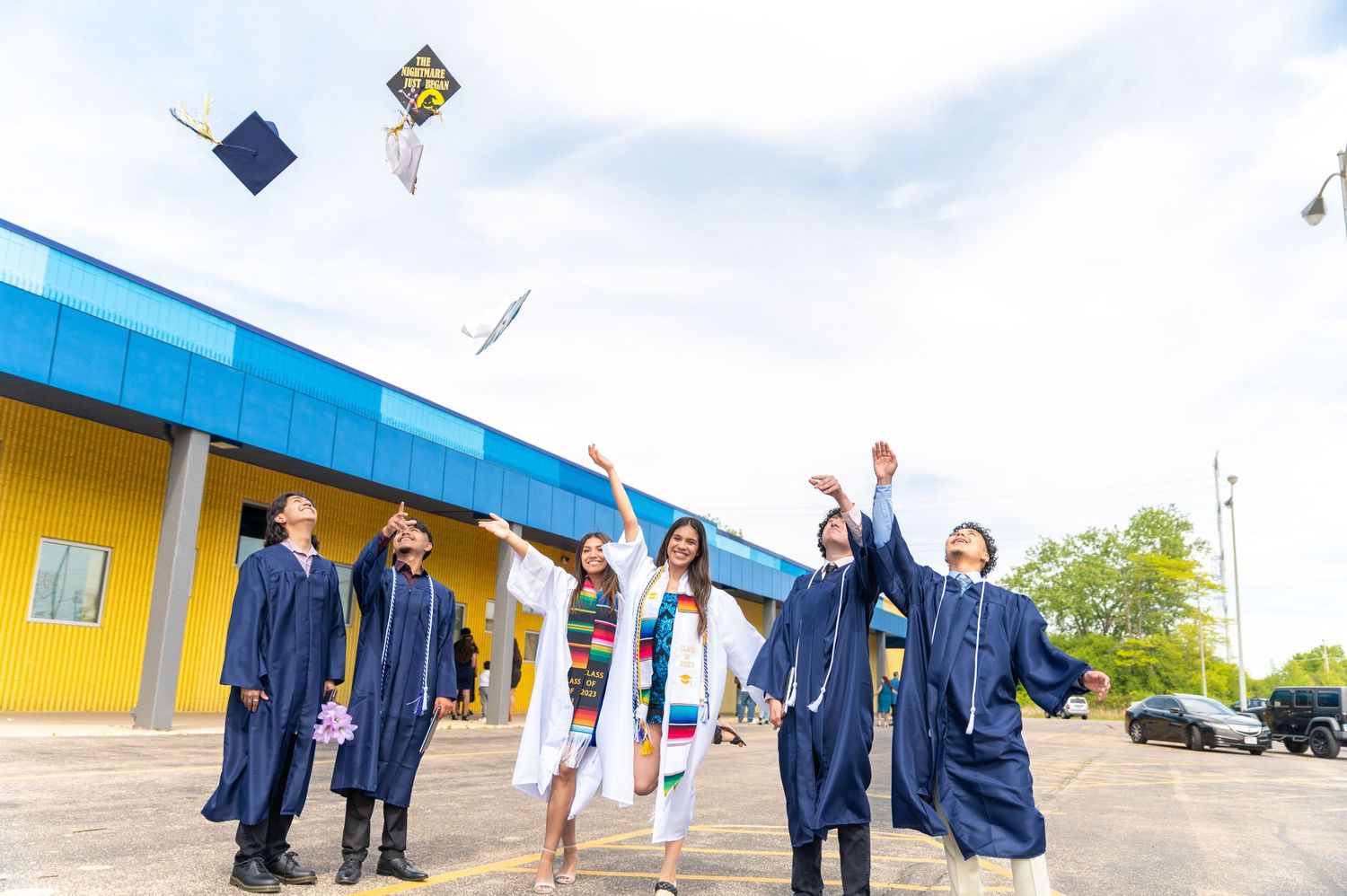 Graduates throwing caps in the air while celebrating in blue gowns outside.