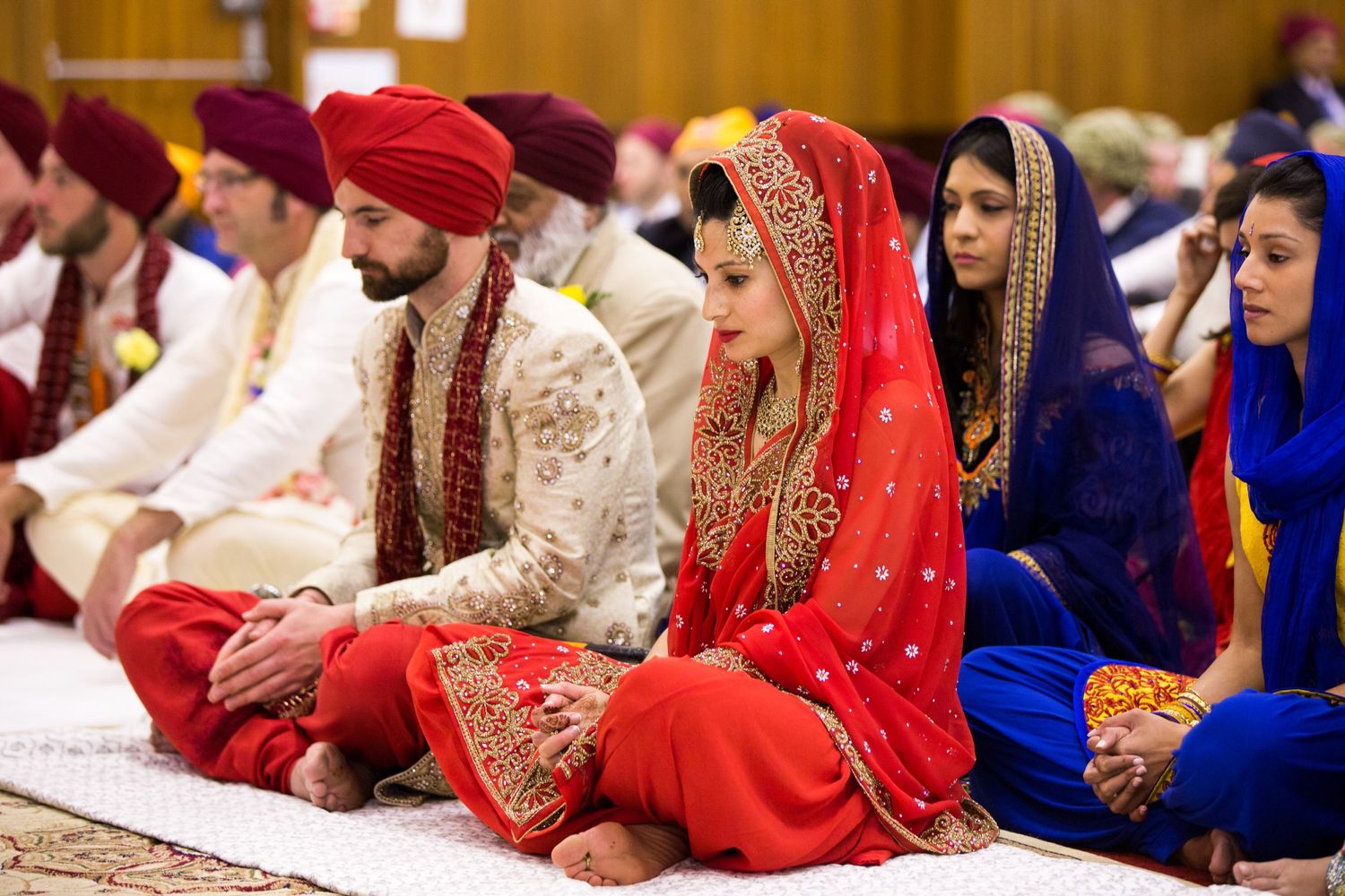 Traditional Sikh wedding ceremony with guests in vibrant red and blue attire seated during religious rituals.