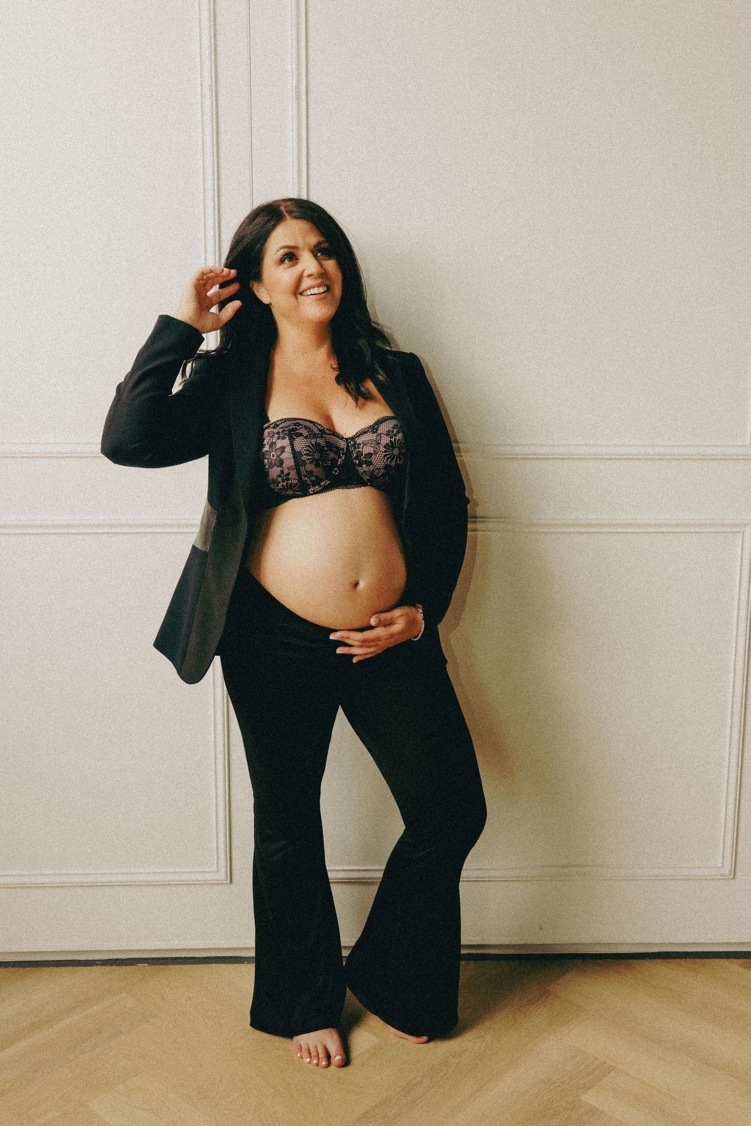 A maternity portrait showing a person in black attire against a white wall.