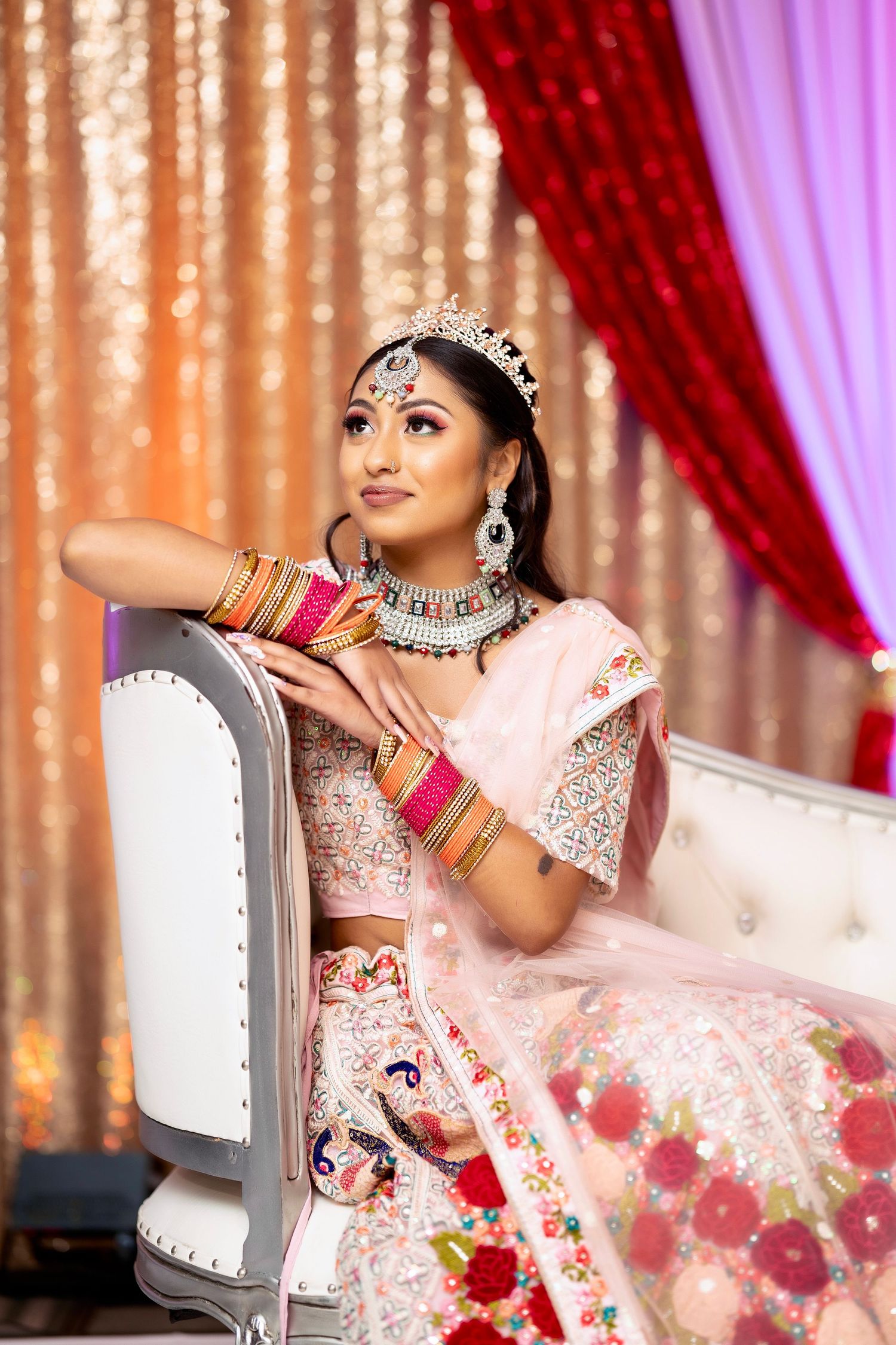 Close-up portrait of bride in traditional Indian attire posing with jewelry against sparkly backdrop.