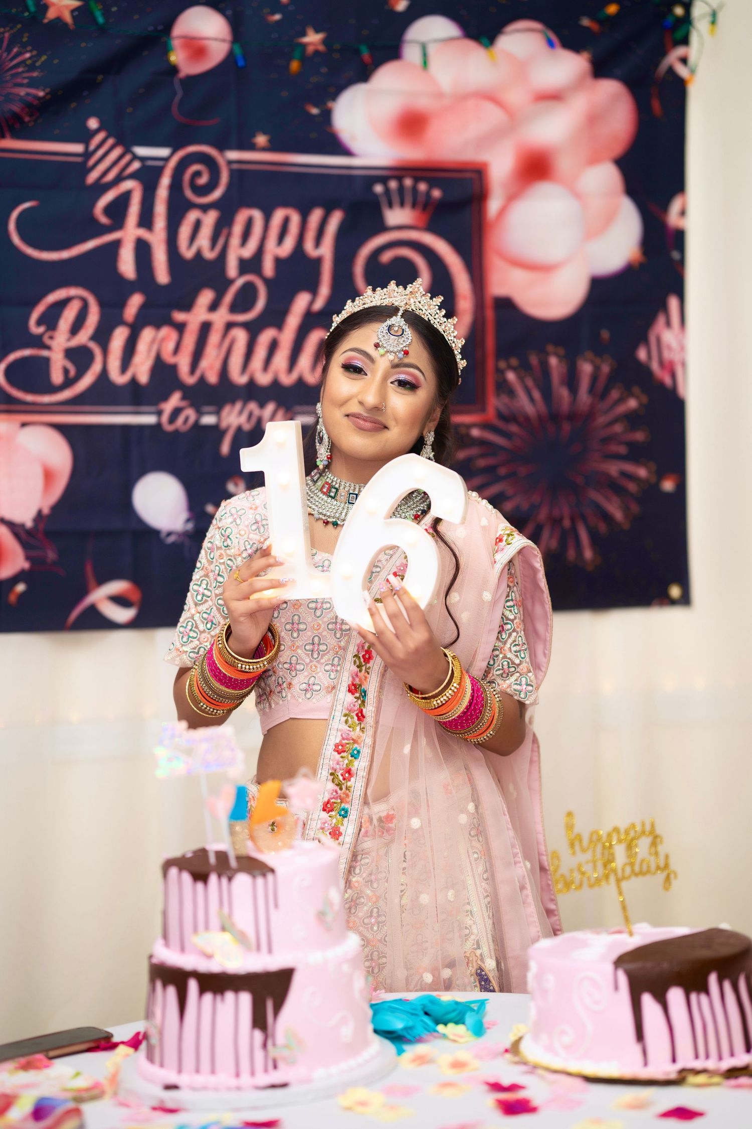 Sweet sixteen celebration with pink cakes and balloons against festive birthday backdrop.