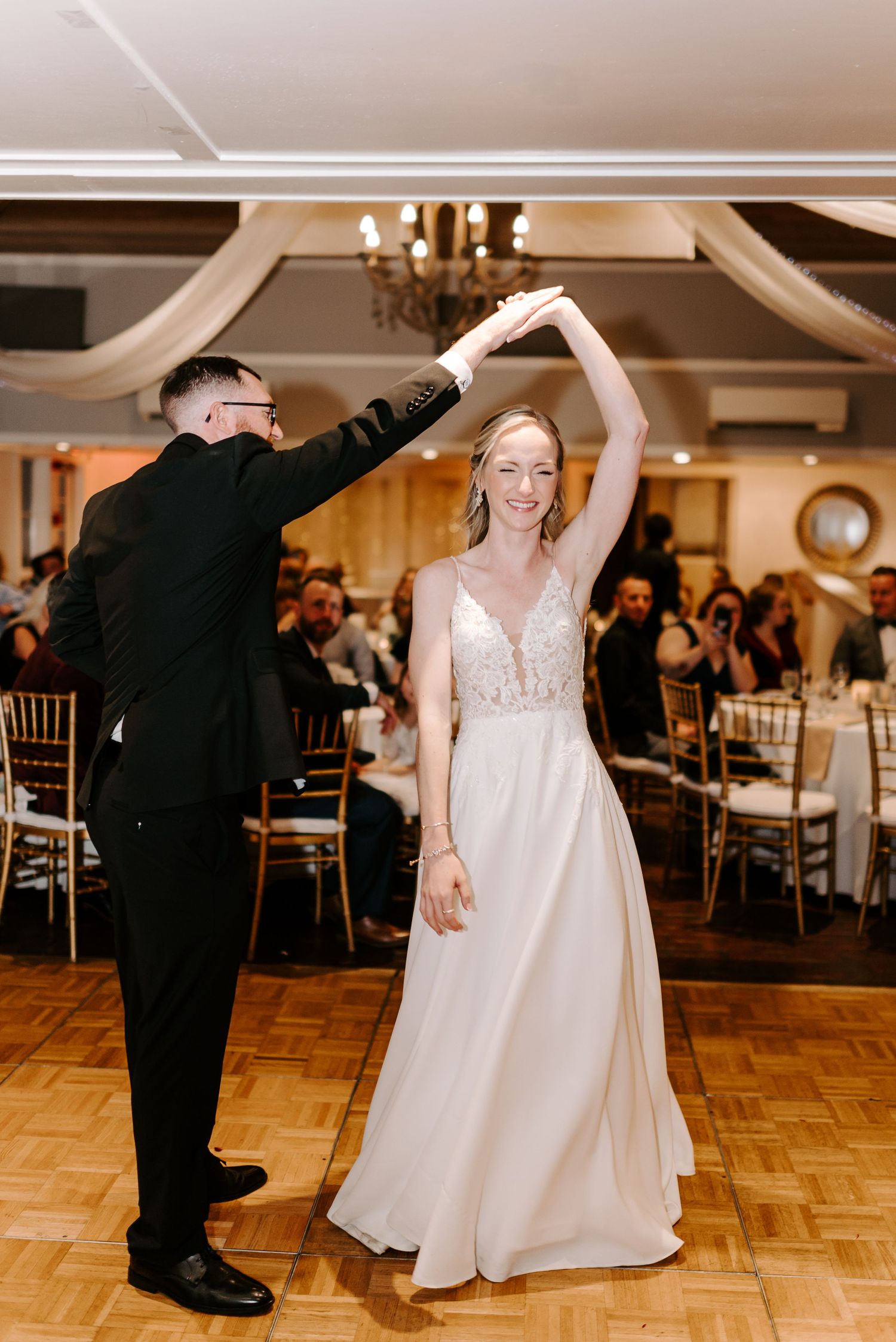 Wedding couple performs a romantic dance on a wooden floor in an elegant reception venue.