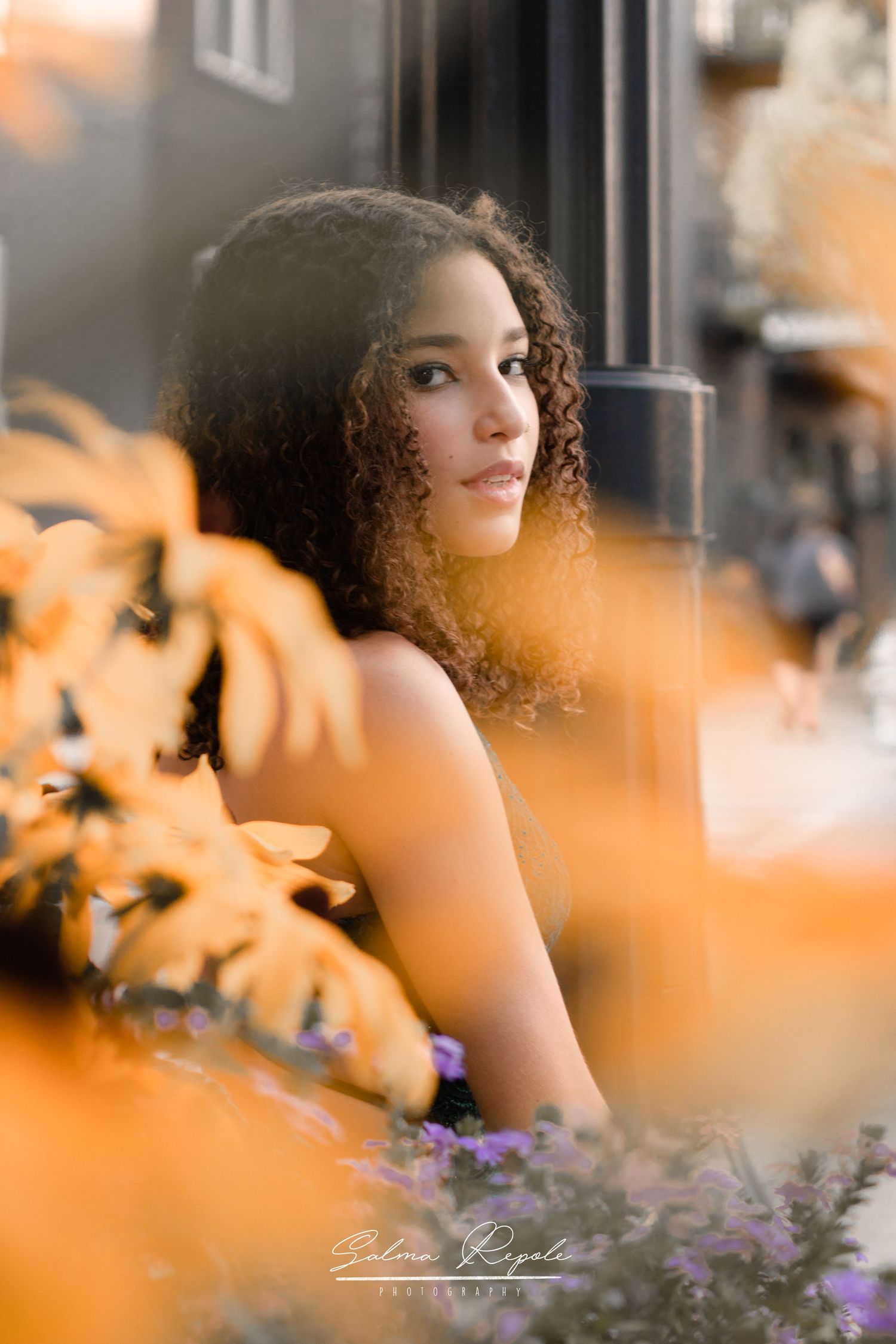 Artistic portrait through orange flowers with soft bokeh effect.
