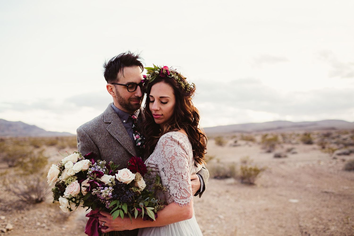 bride with flowers looks down as groom embraces