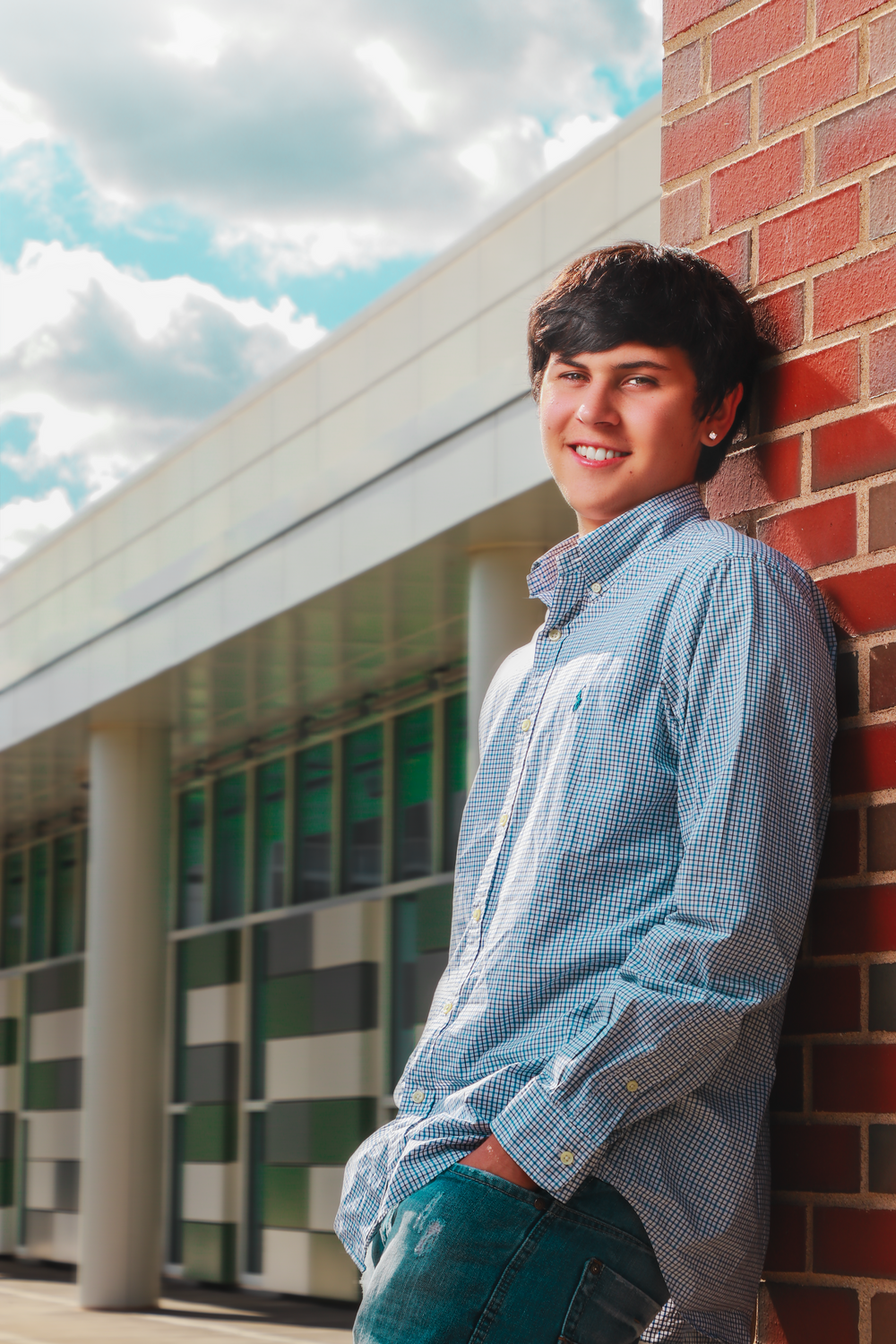 Portrait against brick wall wearing blue checkered shirt near modern building architecture.