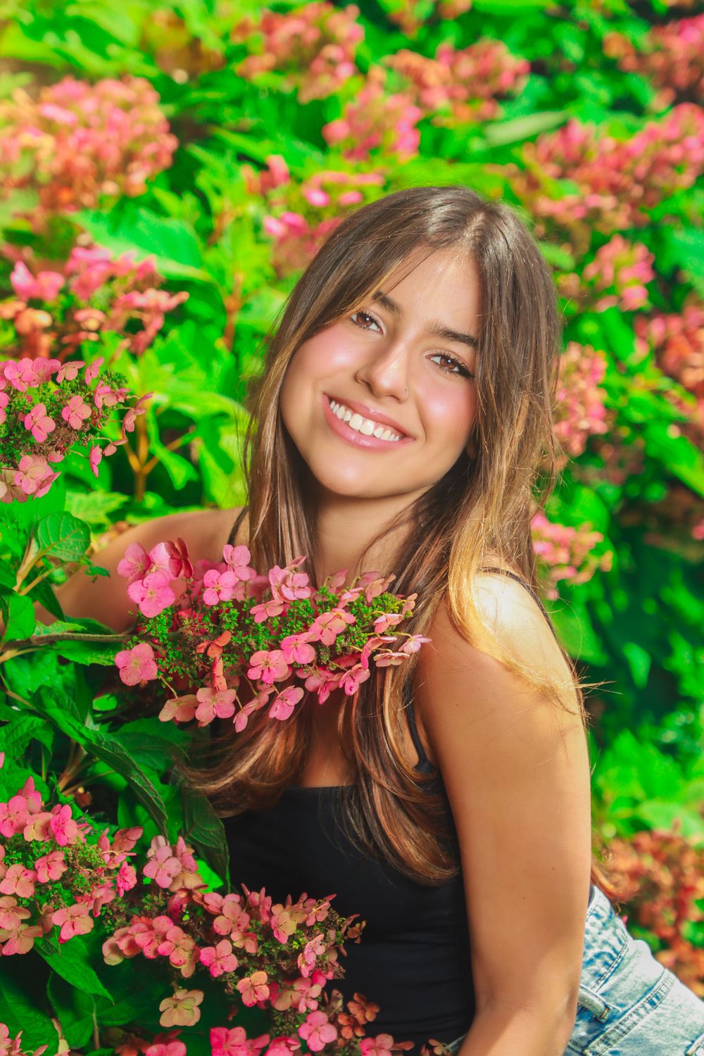 Portrait among pink flowering bushes wearing black top with natural summer garden backdrop.
