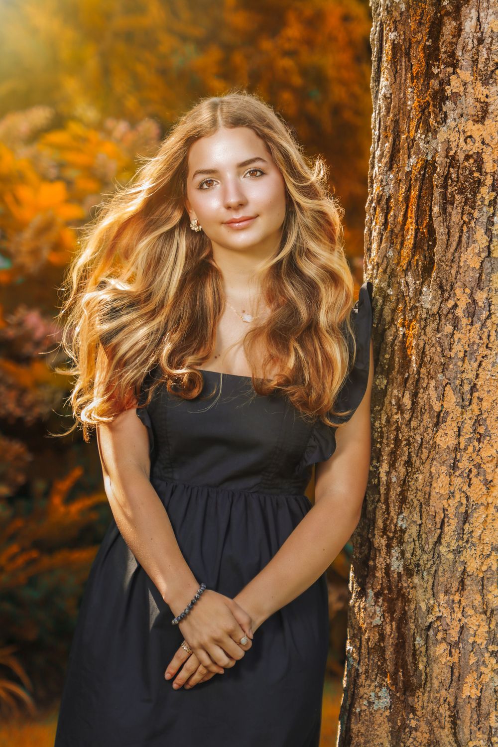 Portrait in a navy dress against autumn foliage with golden sunlight creating a warm glow.