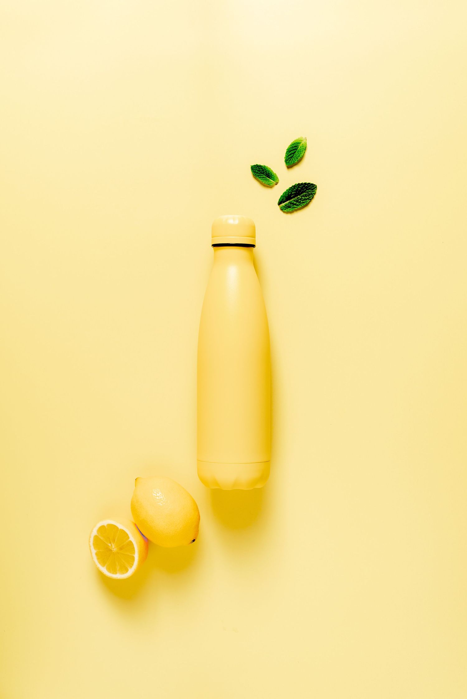 yellow water bottle on a yellow backdrop with lemons and mint to decorate, fresh, minimal and crisp, healthy living