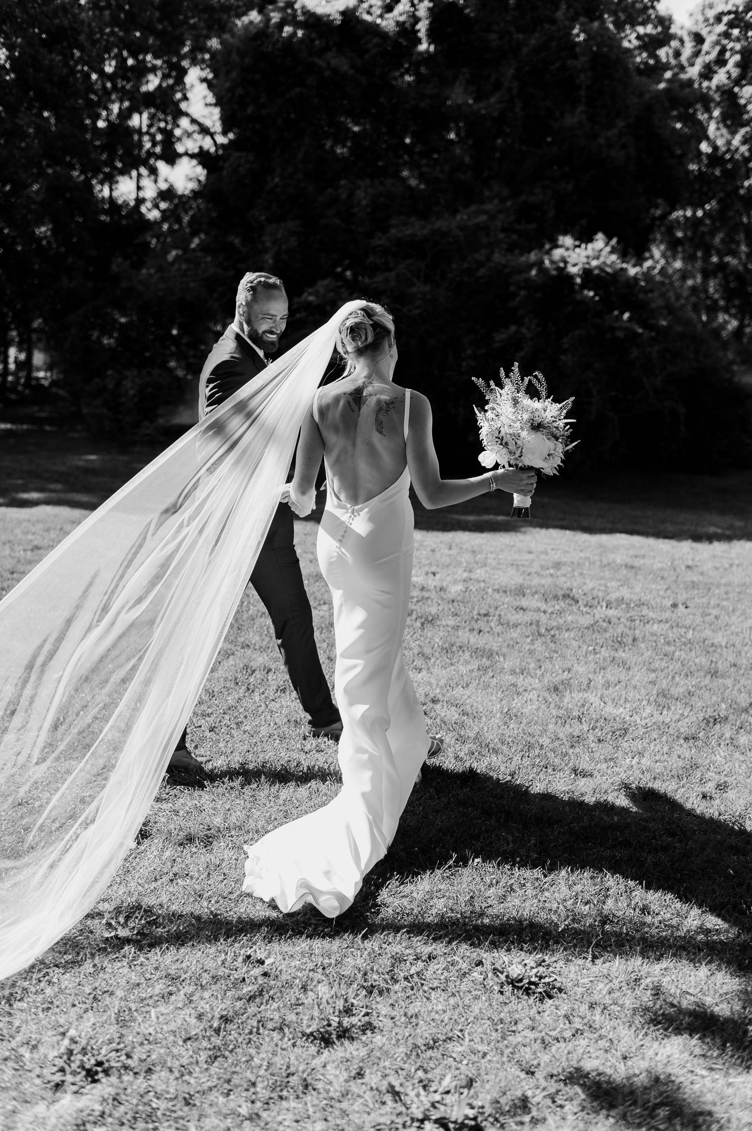 Black and white photo of flowing wedding dress and veil catching the breeze outdoors.