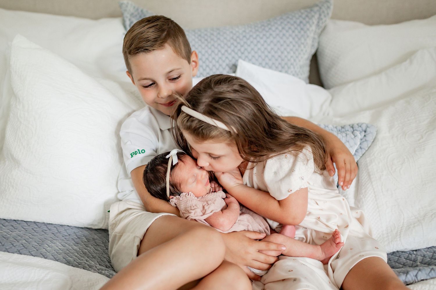 Three people cuddled close together on a white bed showing affection.