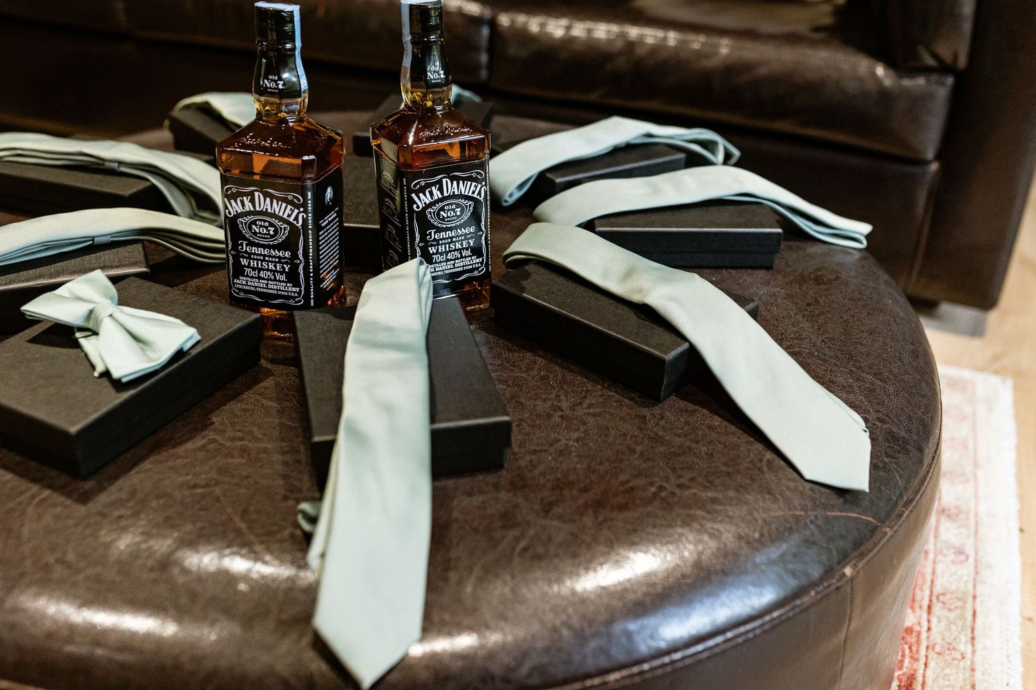 White neckties and two bottles of Jack Daniel's whiskey arranged on a brown leather couch or chair.