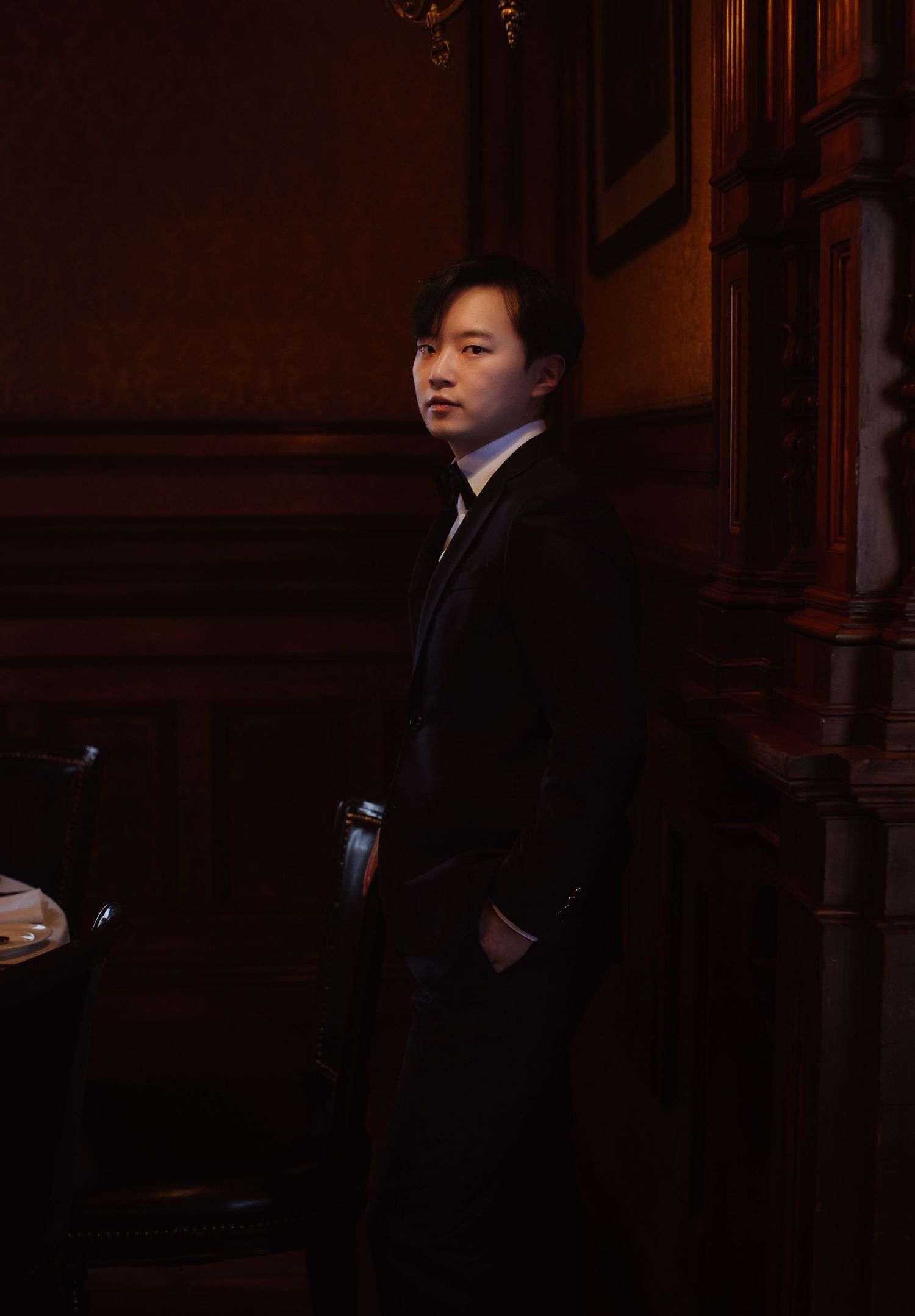 Groom in dark suit standing in richly wood-paneled room.