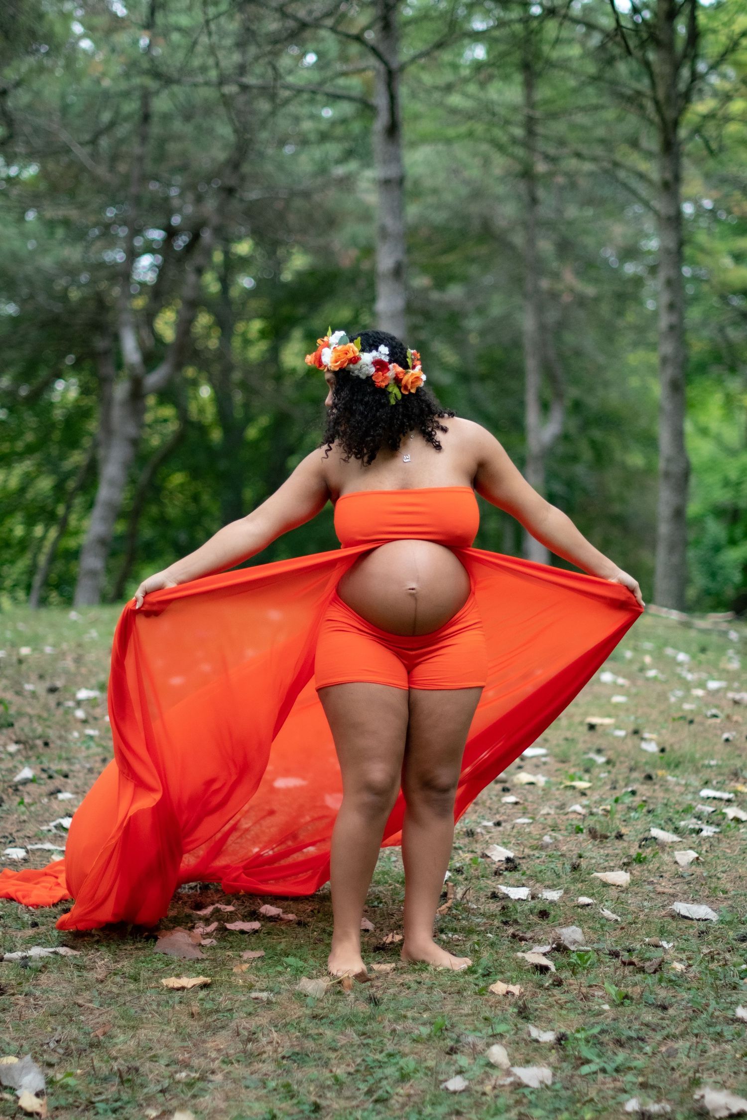 Artistic maternity shoot in wooded area with flowing orange dress.
