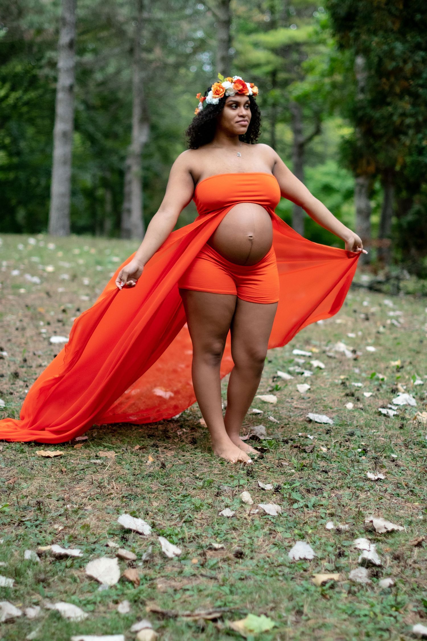 Dramatic maternity photography with flowing orange fabric in forest setting.