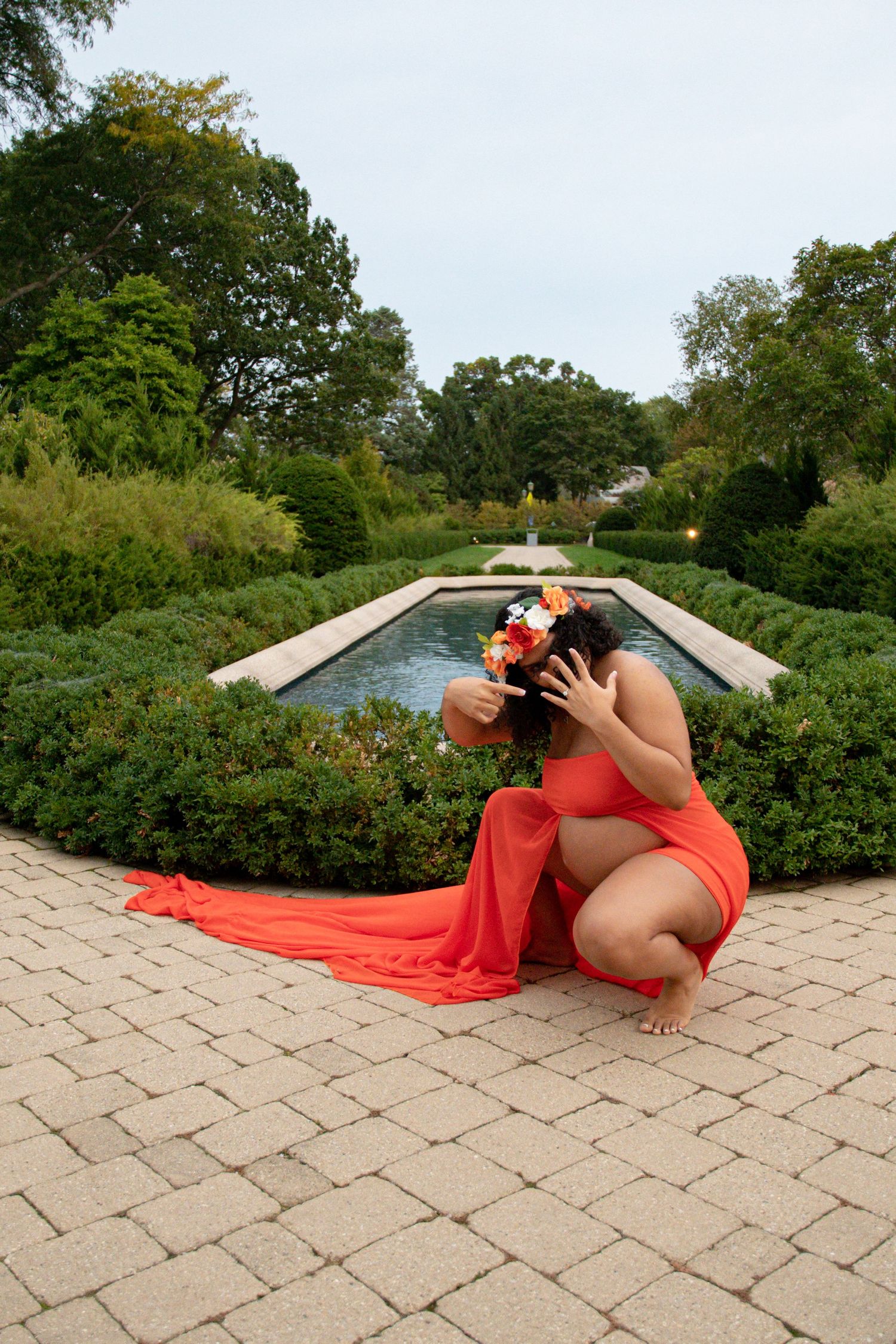 Maternity photo session on stone patio with orange flowing fabric and garden background.